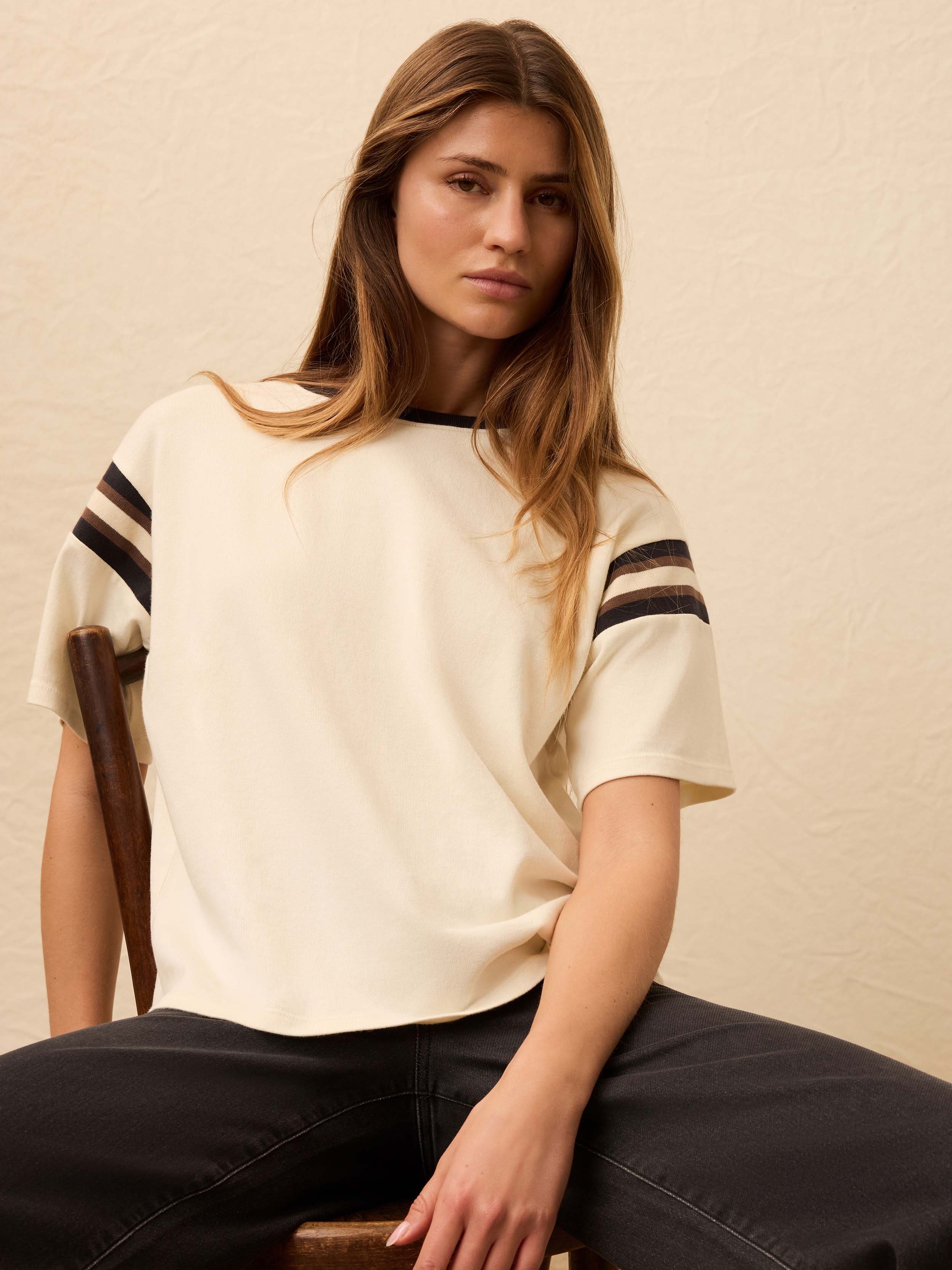 Woman is wearing a white sport jersey tee with black jeans against a beige background