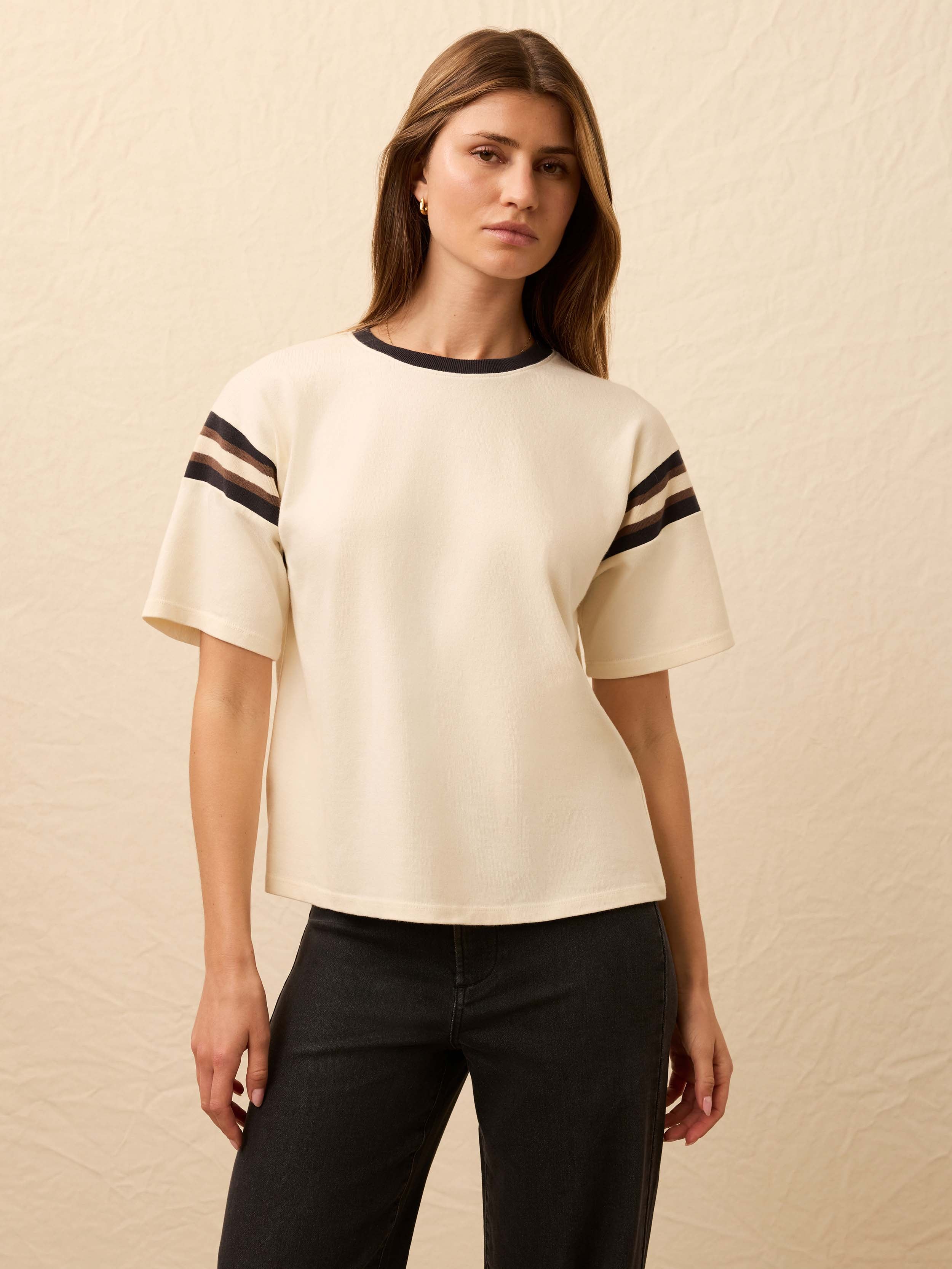 Woman is wearing a white sport jersey tee with black jeans against a beige background