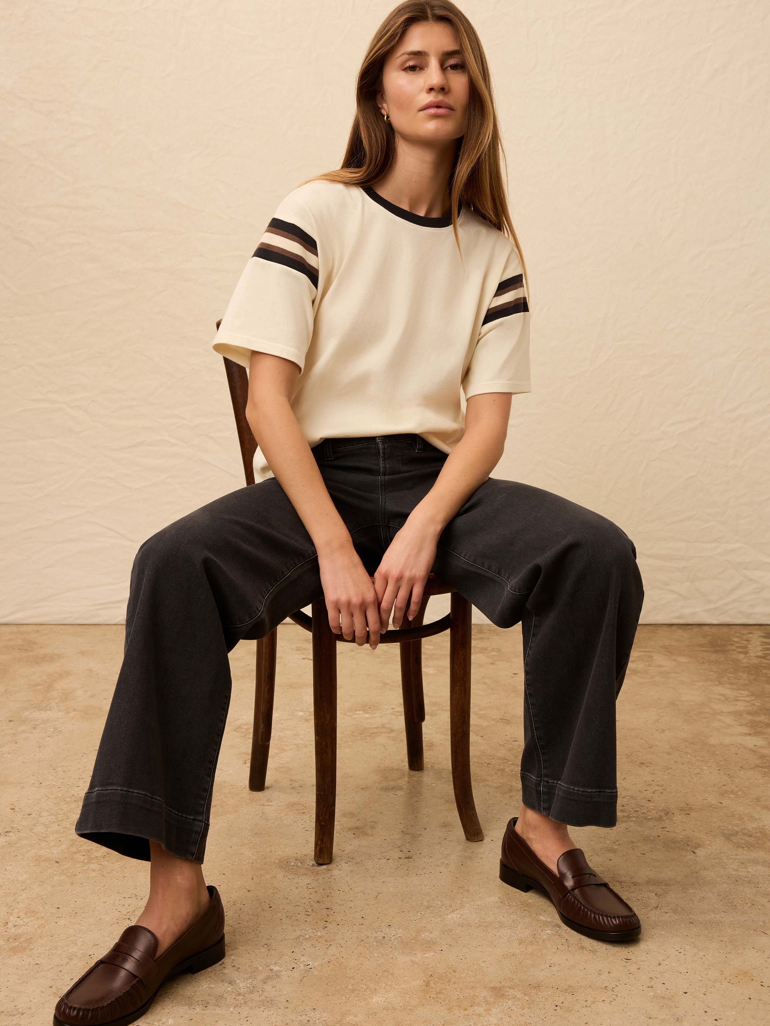 Woman is wearing a white sport jersey with black jeans against a beige background