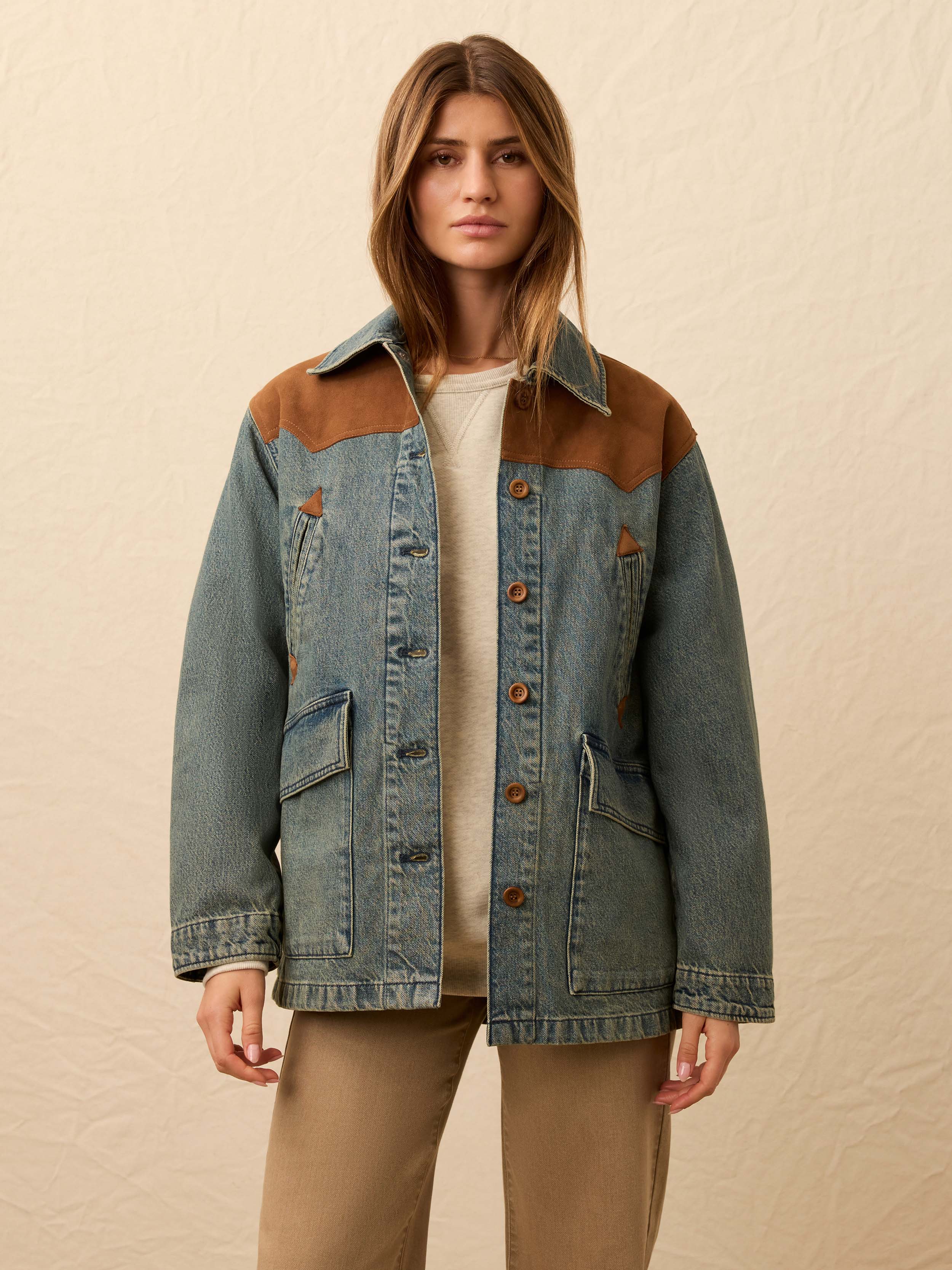 Woman wearing a denim jacket with brown suede accents against a beige background