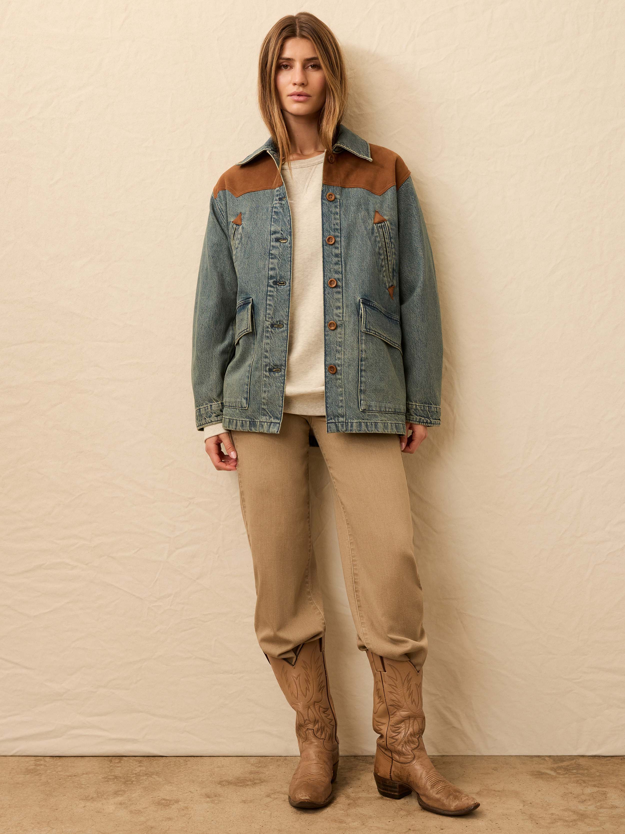 Woman wearing a denim jacket with brown suede accents against a beige wall.
