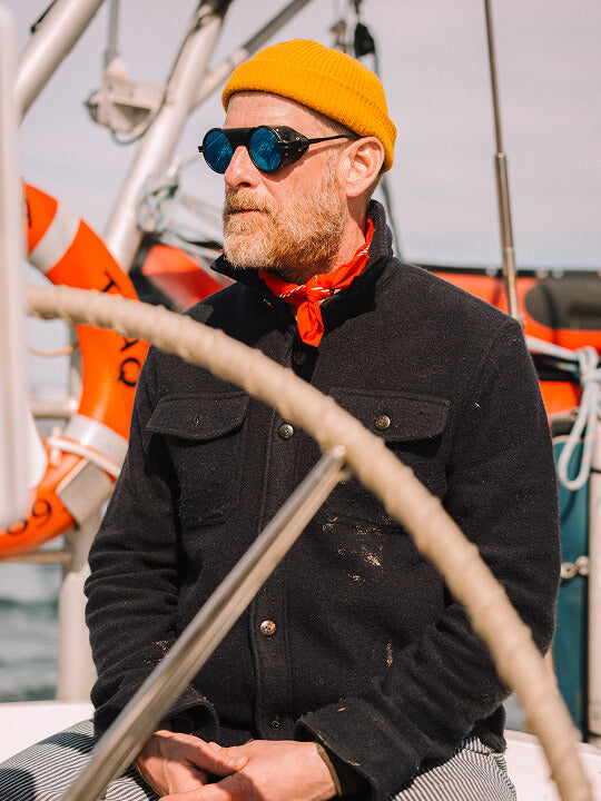 Man sitting at the helm of a sailboat wearing a CPO Jacket