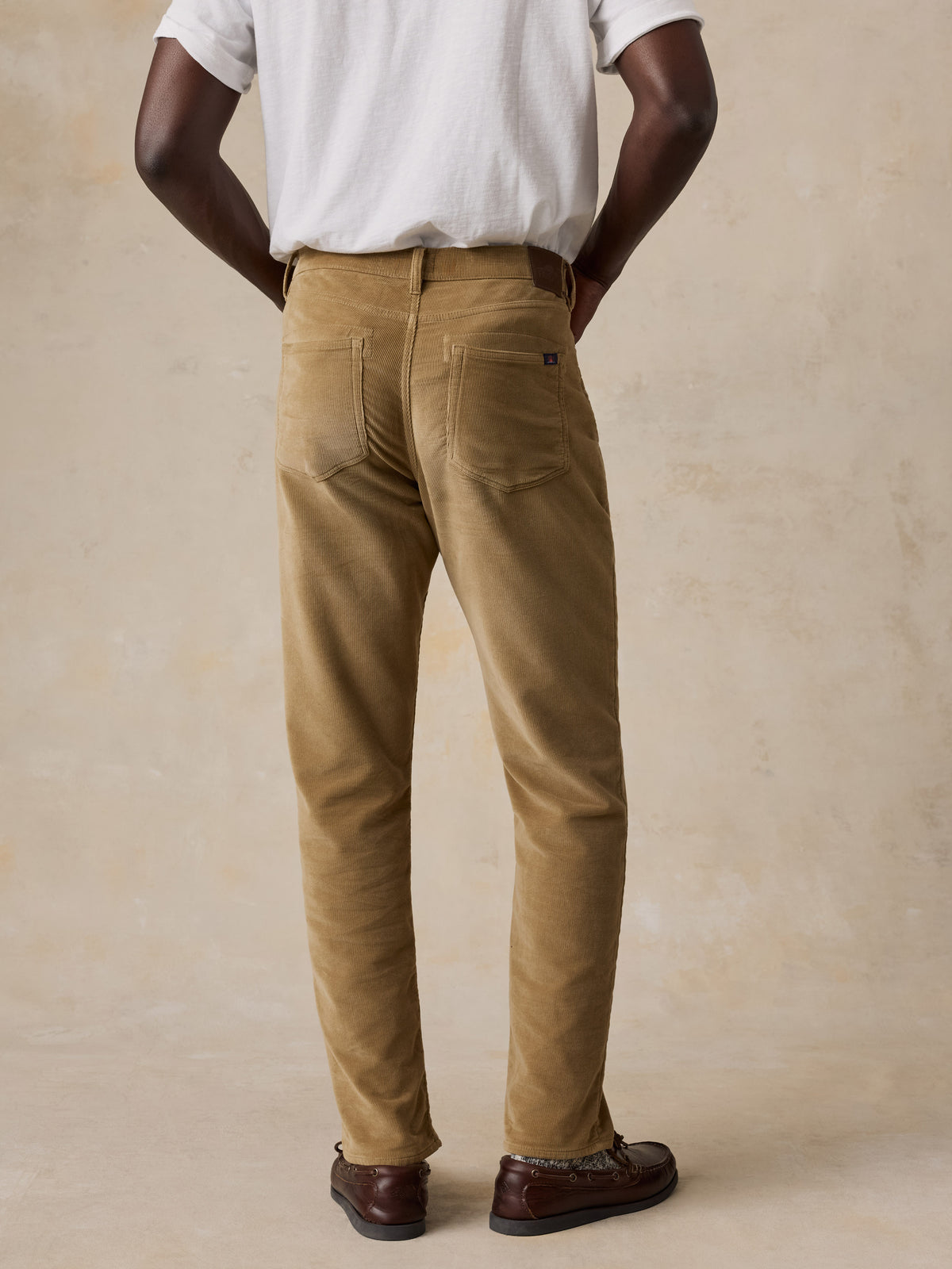 A man viewed from behind wearing a white tee and tan corduroy pants, image 3 of 5