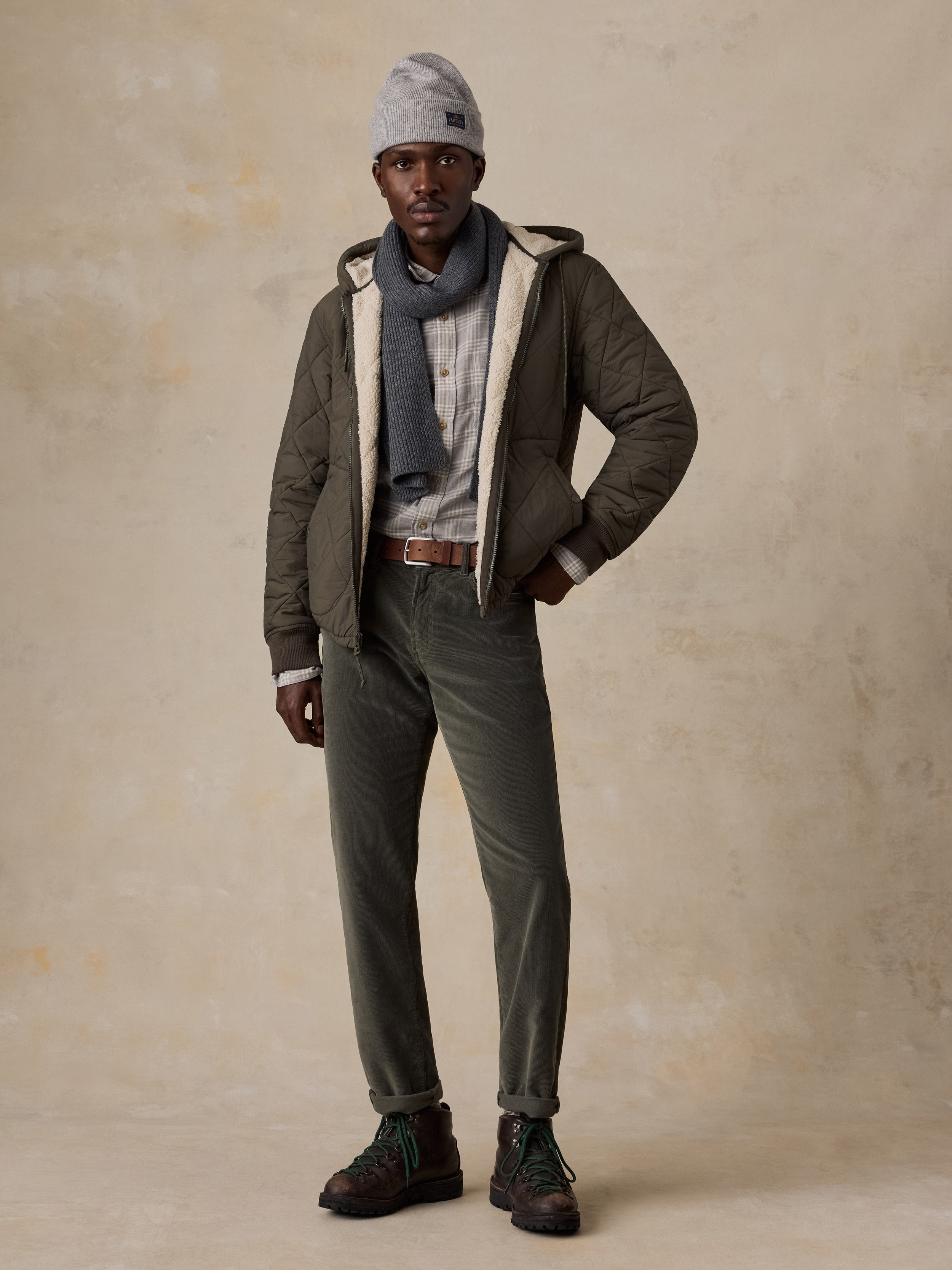 A man wearing green corduroy pants with a plaid button shirt and a quilted jacket