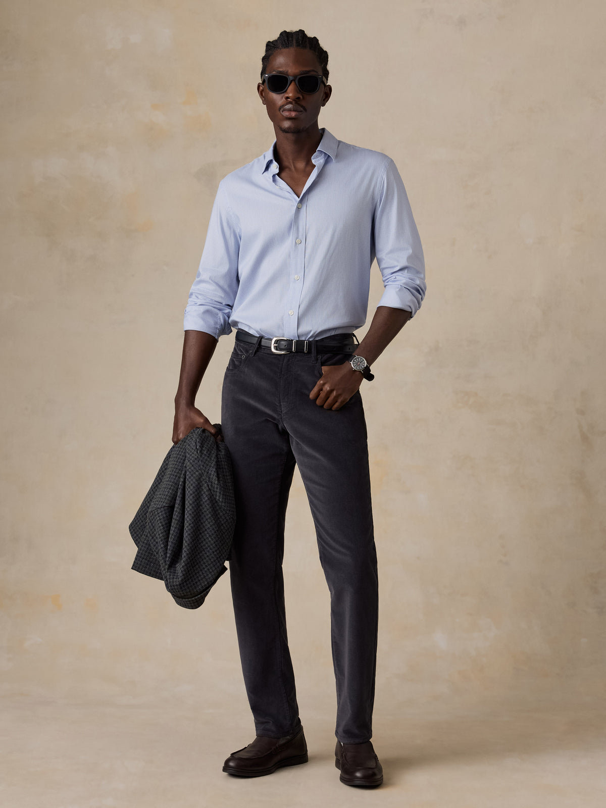 A man wearing a blue button down shirt with grey corduroy pants, image 2 of 5