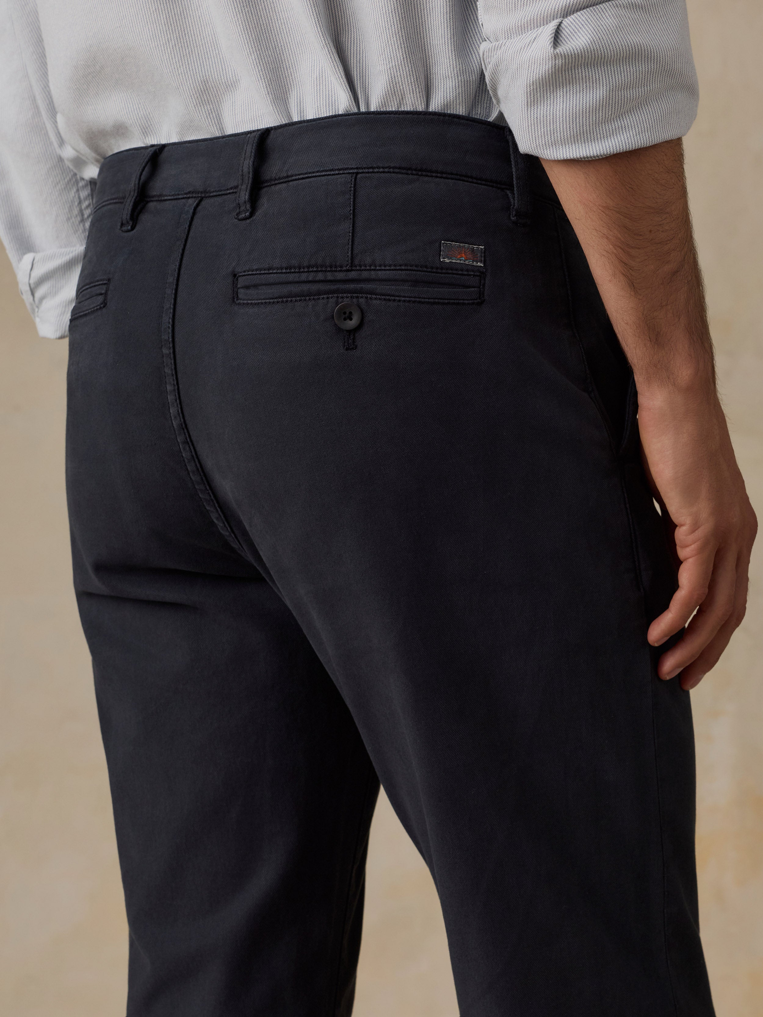 Close-up back view of a man wearing dark charcoal gray trousers with a light-colored shirt tucked in, showing the waistband, belt loops, and back pocket details.
