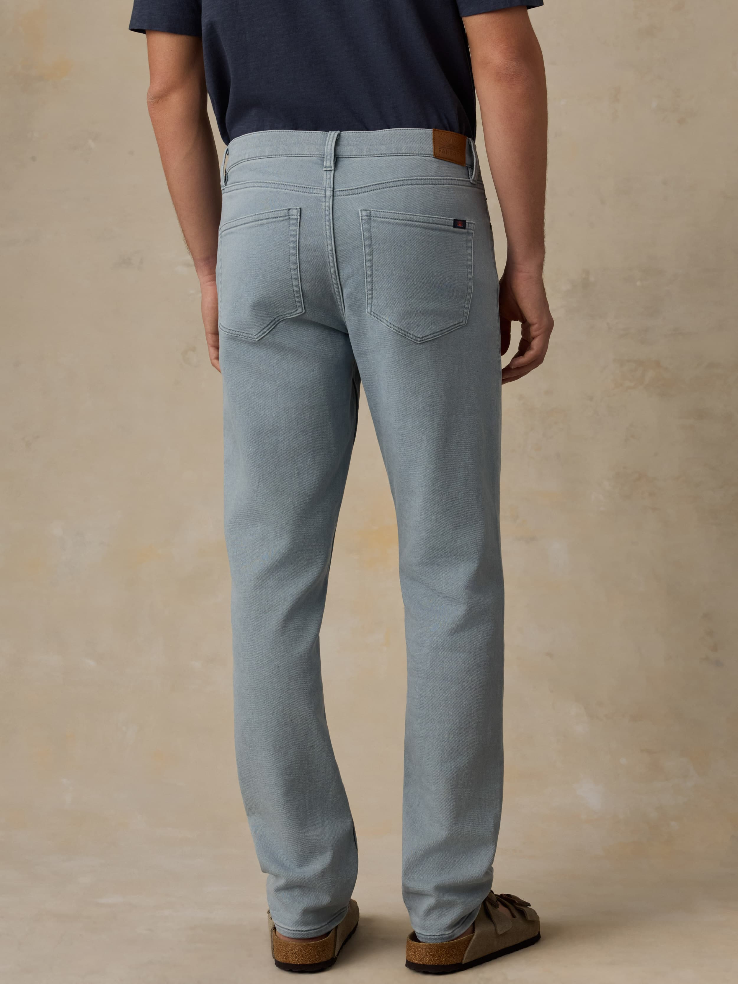 Man wearing light blue pants and a navy shirt on a beige background