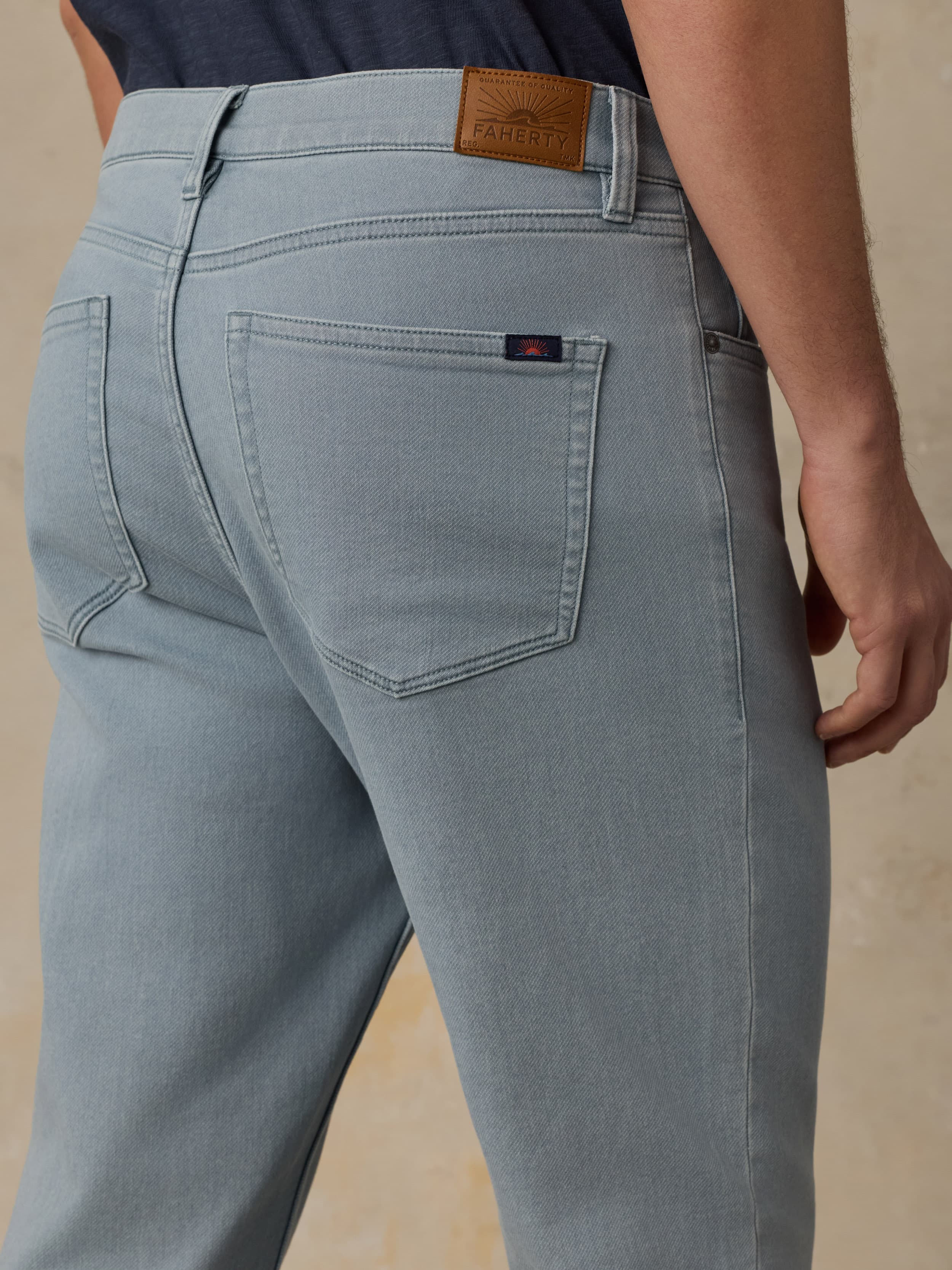 Man wearing light blue pants and a navy shirt on a beige background