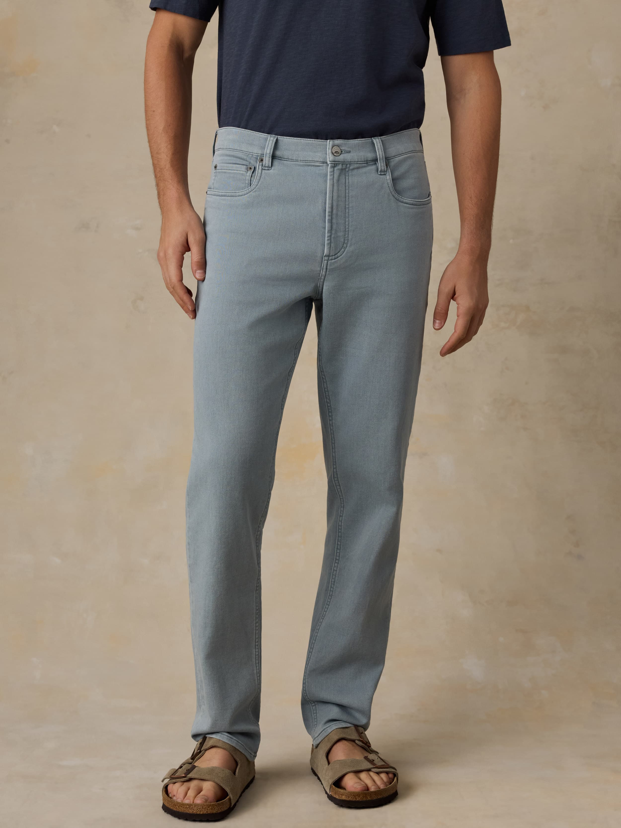 Man wearing light blue pants and a navy shirt on a beige background