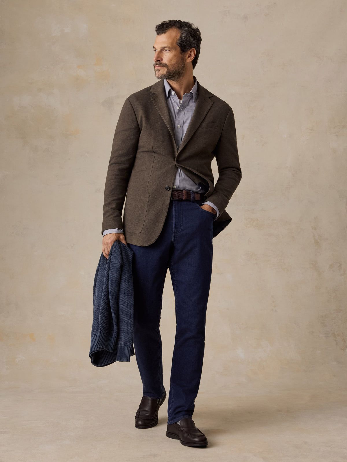 A man wearing a brown blazer, blue jeans, and leather shoes, image 5 of 5