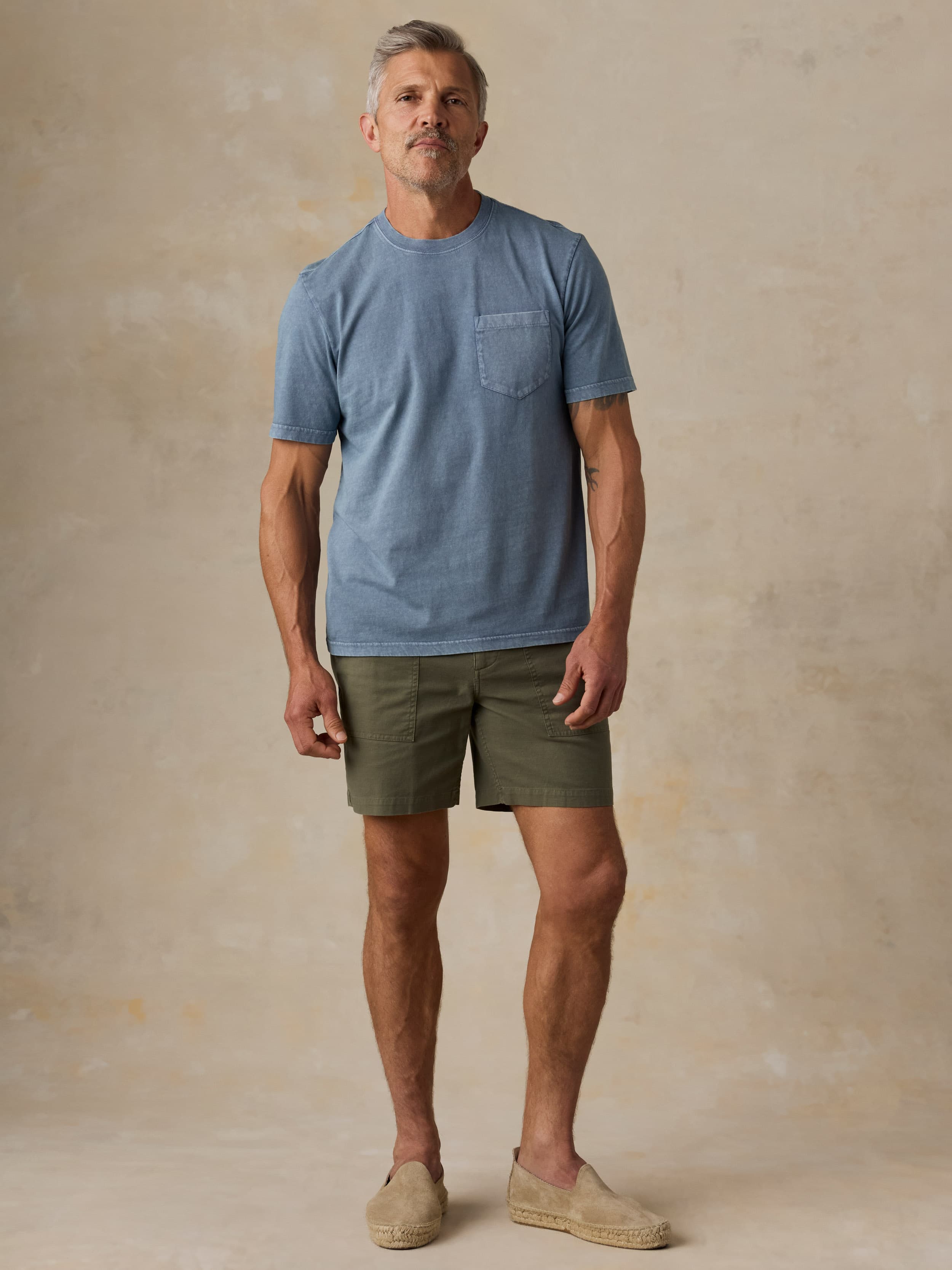 Man wearing a blue t-shirt and green shorts against a beige background