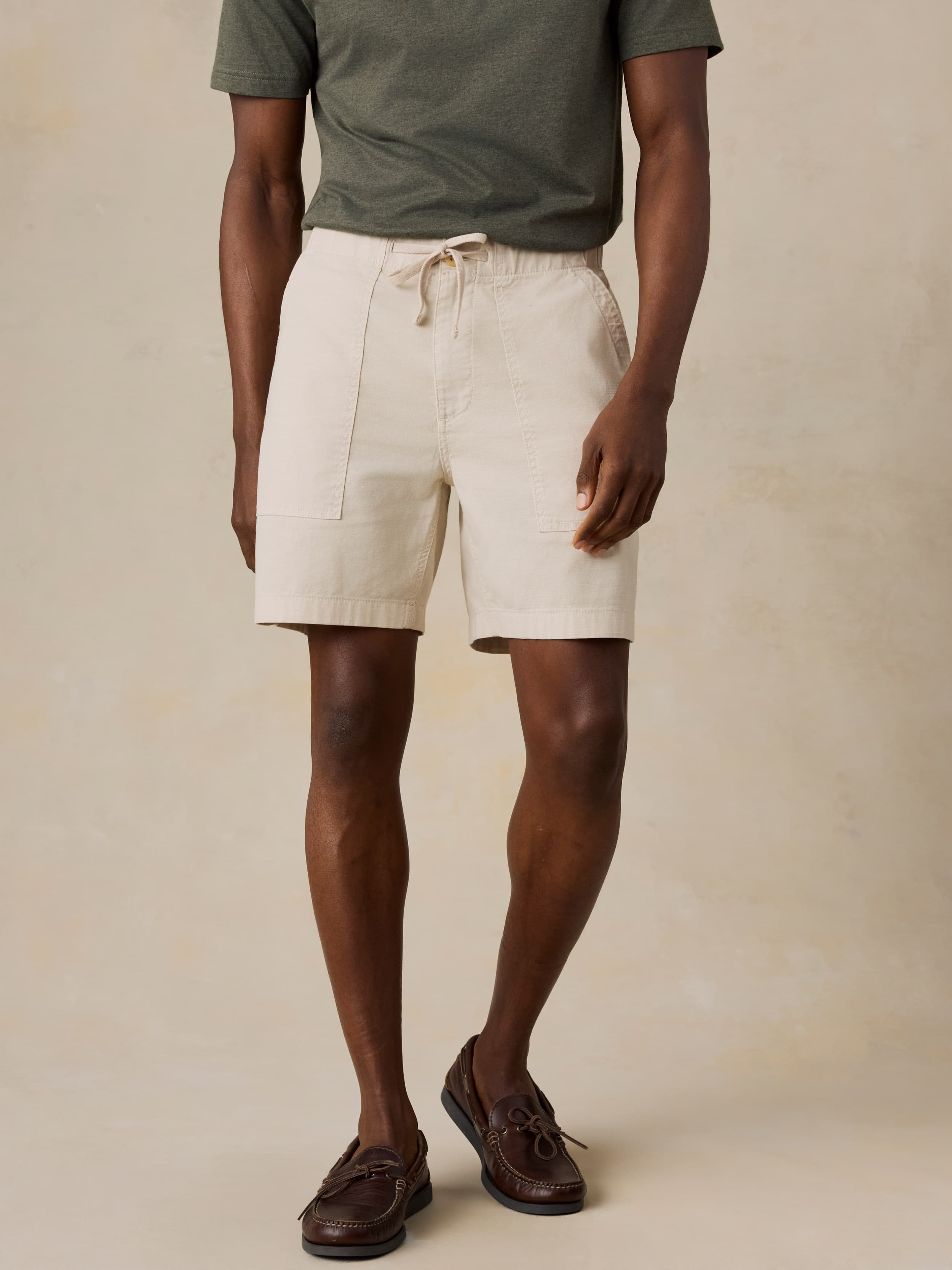 Man wearing beige shorts and a green shirt on a beige background