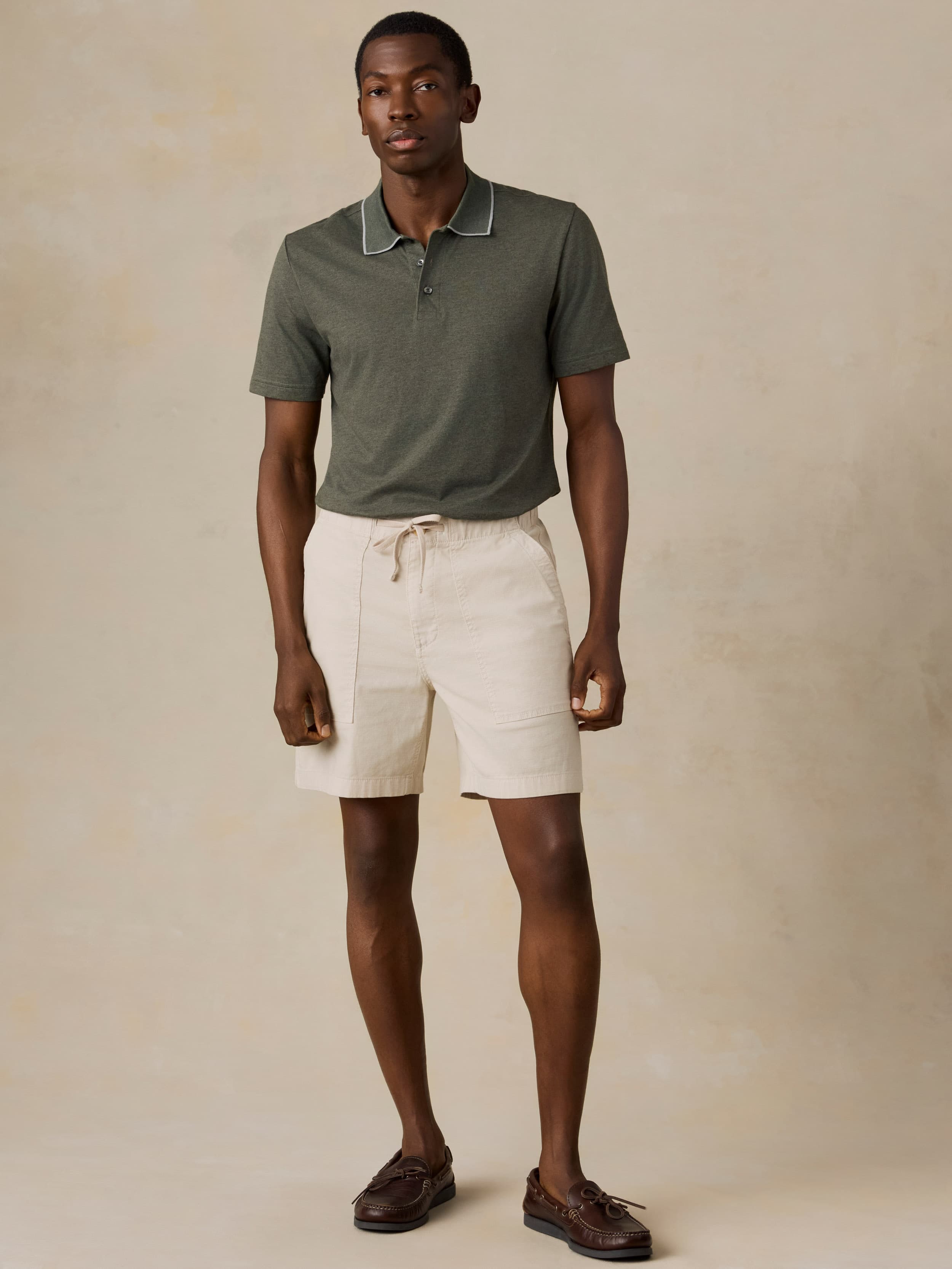 Man wearing a green polo shirt and beige shorts against a beige background