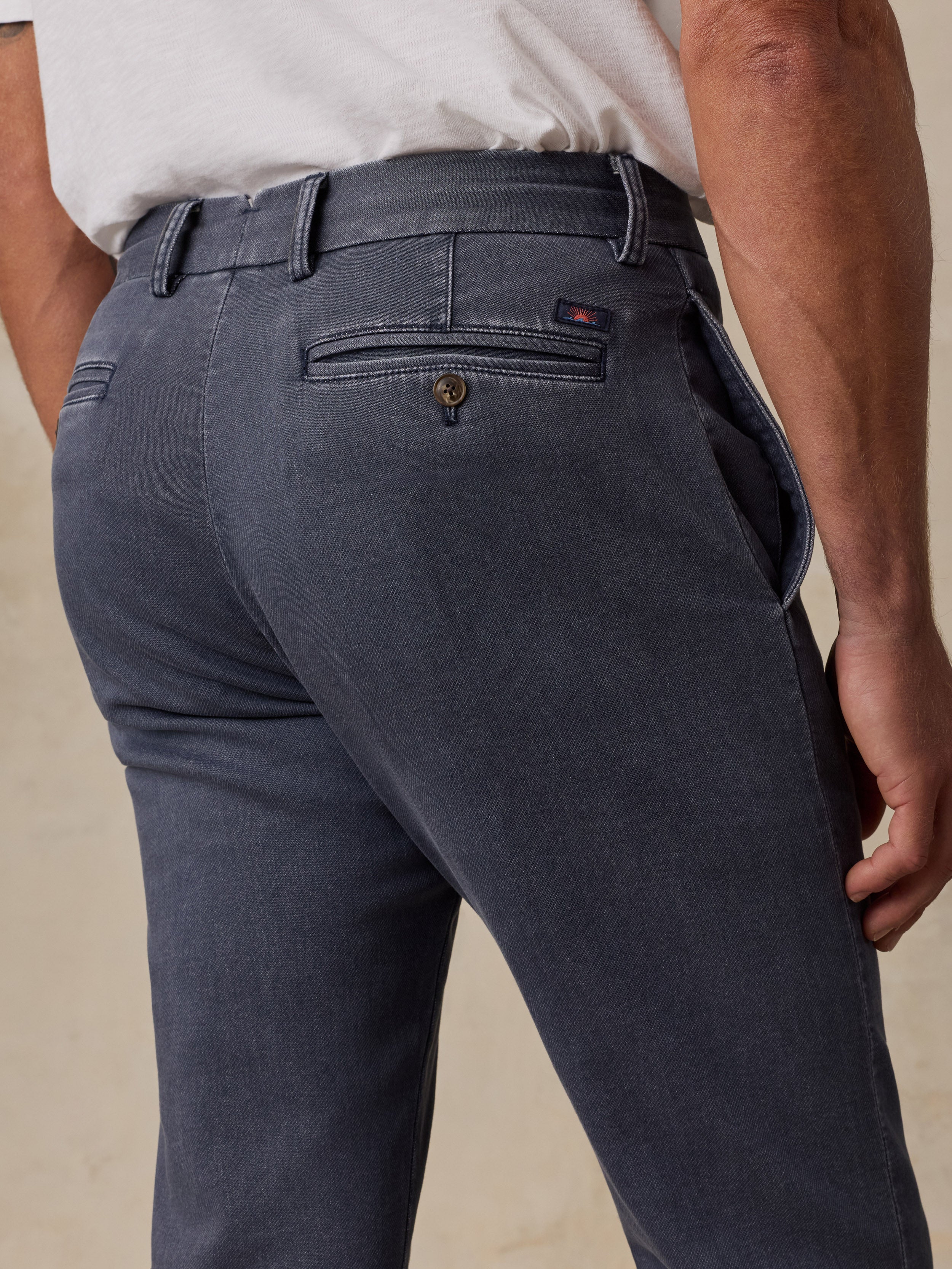 Close-up back view of a man wearing dark charcoal gray slim-fit trousers, showing the waistband, belt loops, back pocket, and a small red Tommy Hilfiger logo tab.