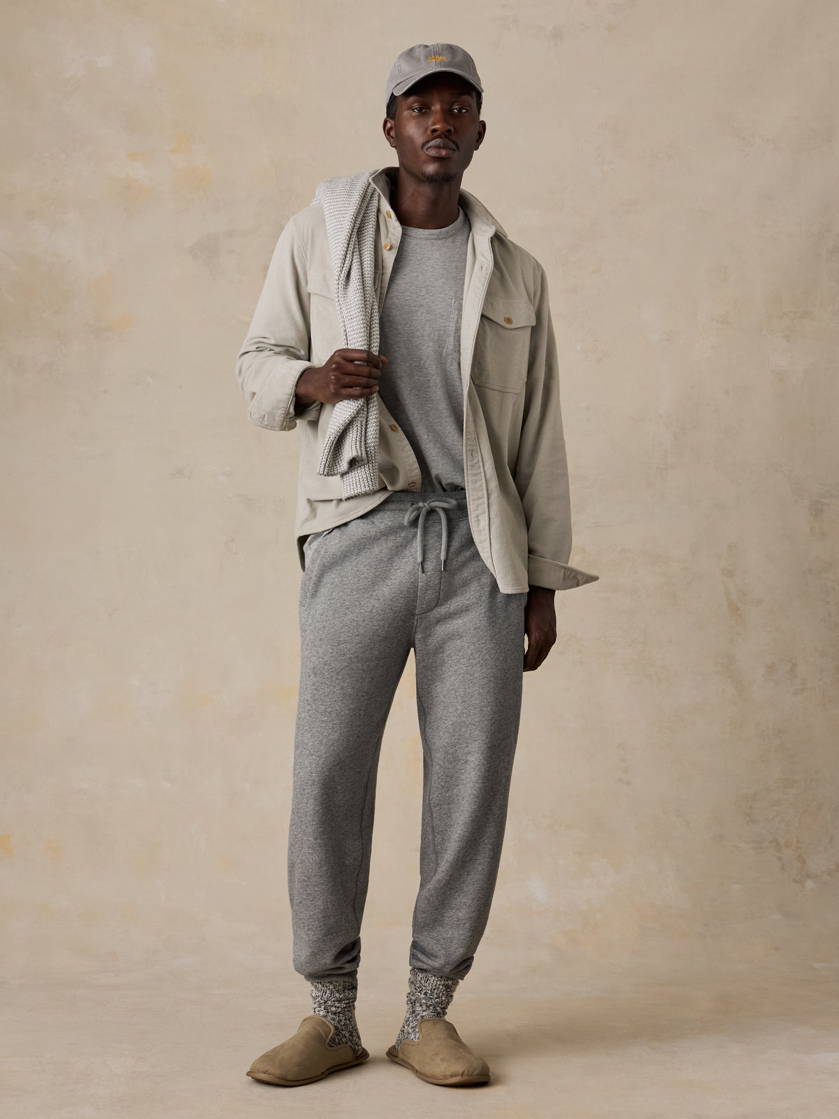 A man wearing grey sweatpants, a grey t-shirt, and a beige overshirt, image 1 of 5
