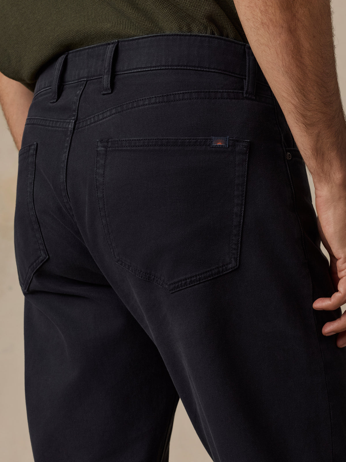 Close-up back view of a person wearing dark navy jeans, showing the waistband, belt loops, back pockets, and a small red Faherty brand tab on the pocket., image 2 of 6