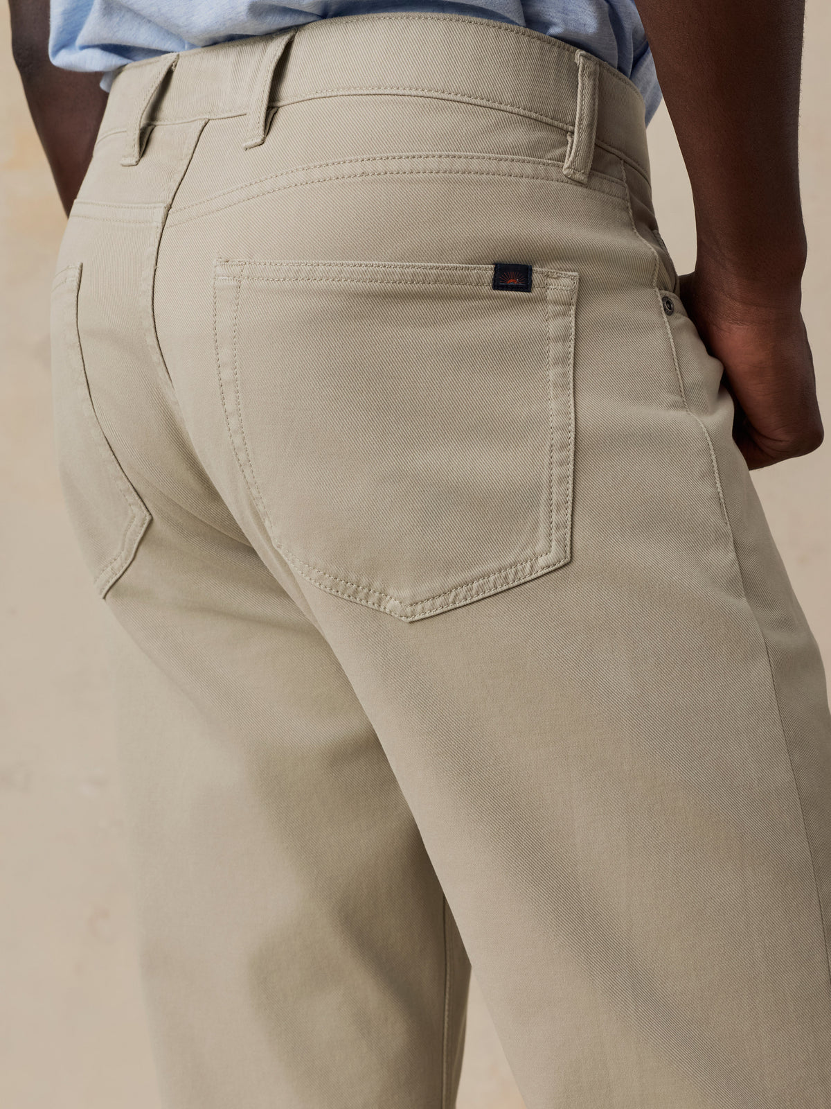 Close-up back view of a person wearing light beige chinos or casual trousers, showing the back pocket, belt loops, waistband, and part of the blue shirt at the waist., image 3 of 6