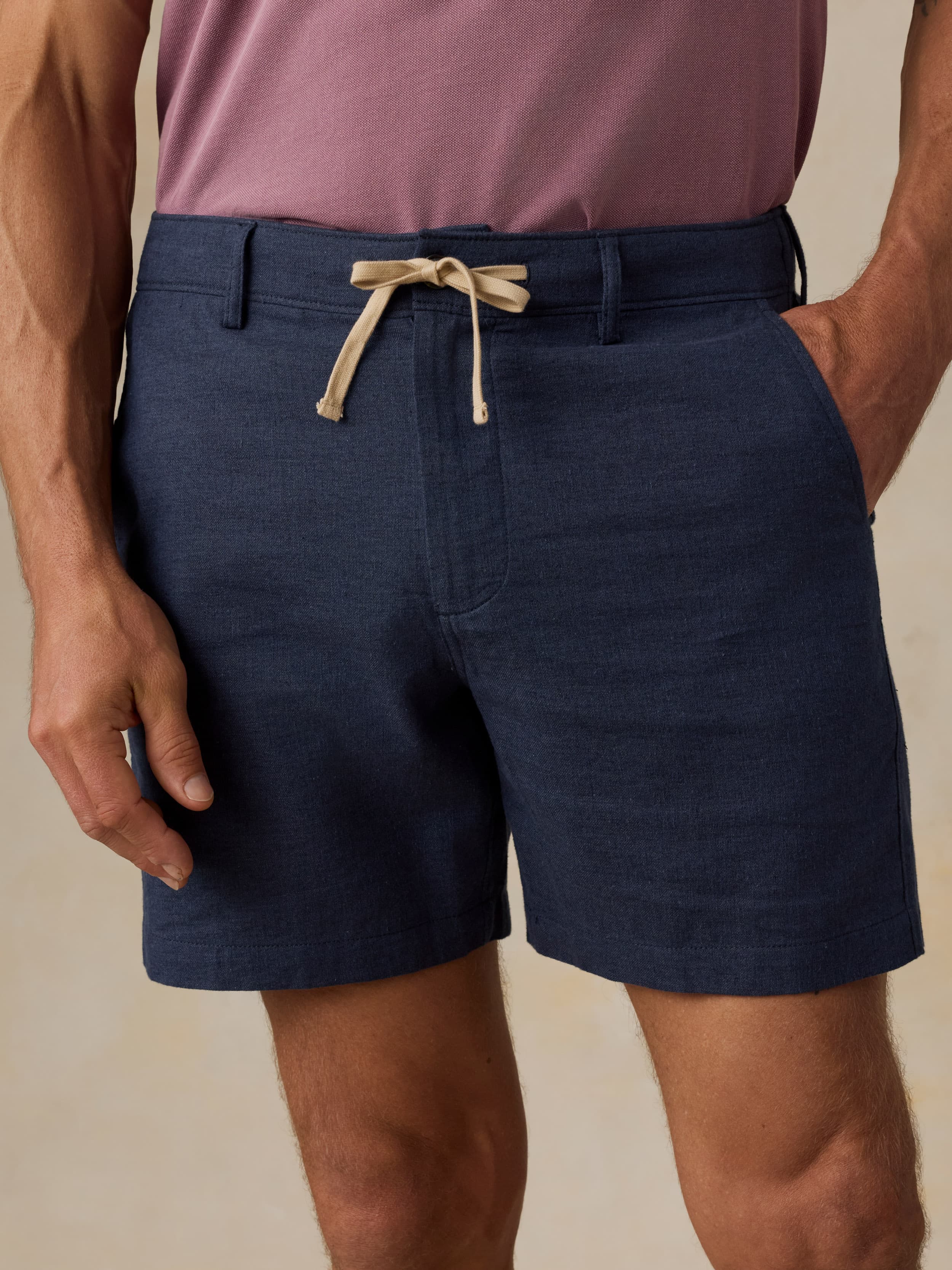 Man wearing navy shorts and a purple shirt on a beige background