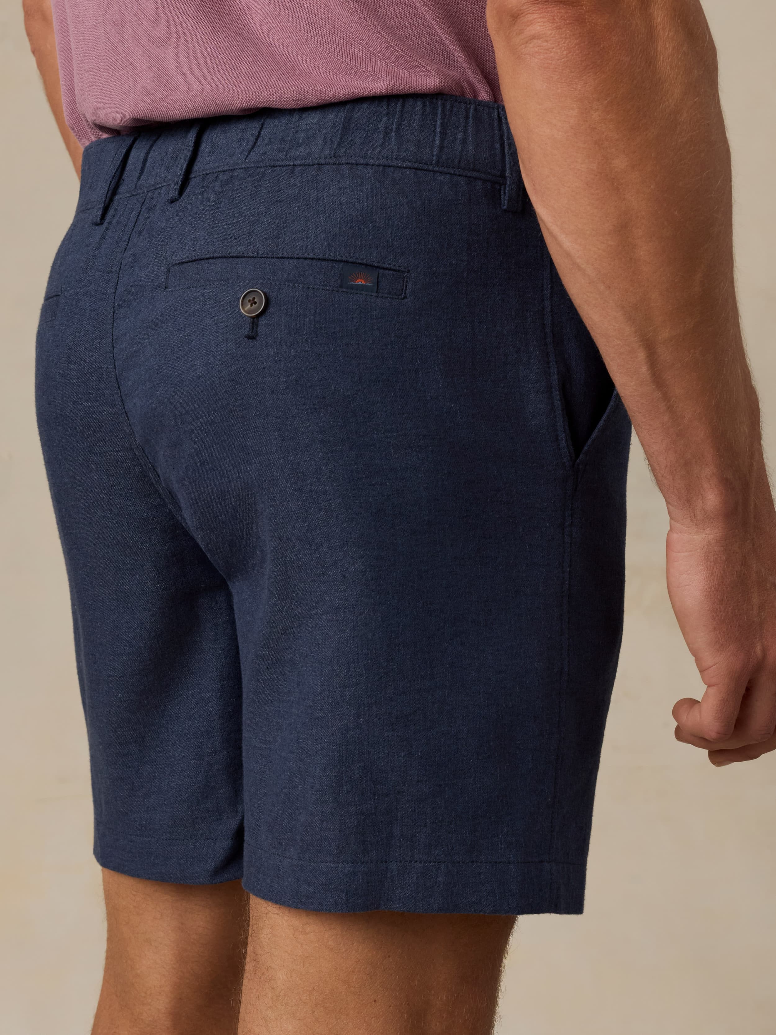 Man wearing navy shorts and a purple shirt on a beige background