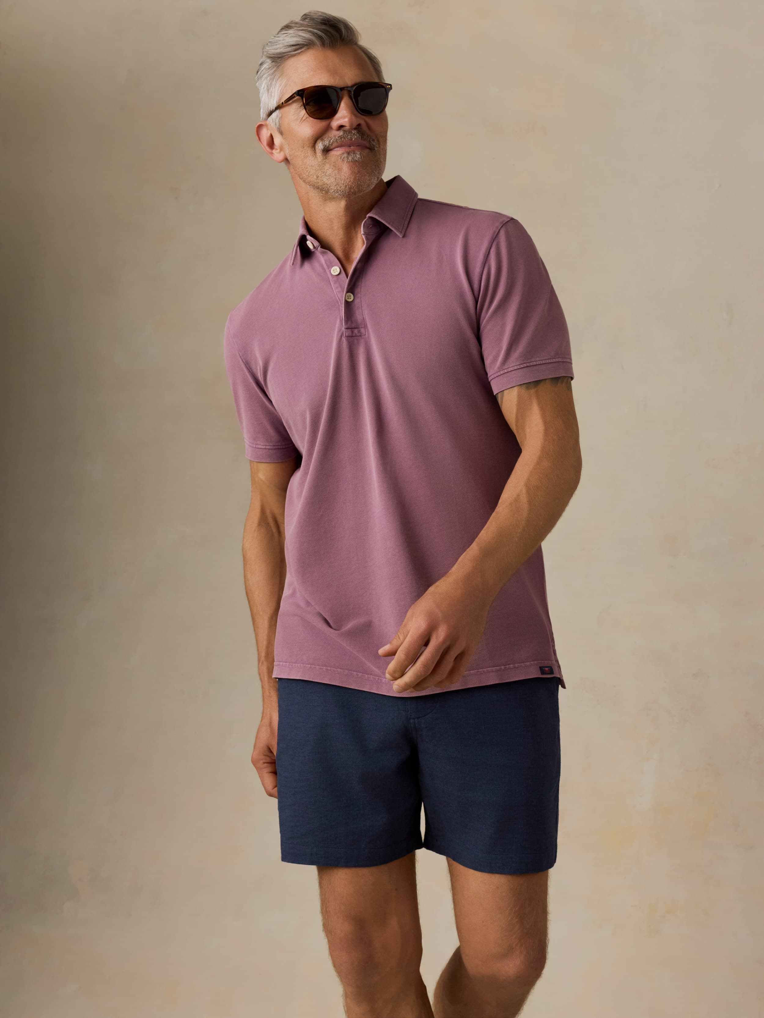 Man wearing navy shorts and a purple shirt on a beige background