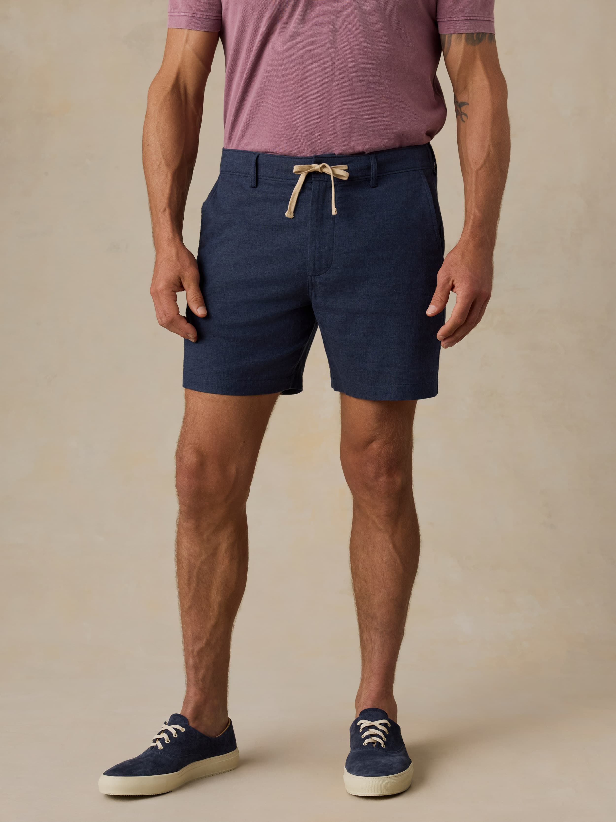 Man wearing navy shorts and a purple shirt on a beige background