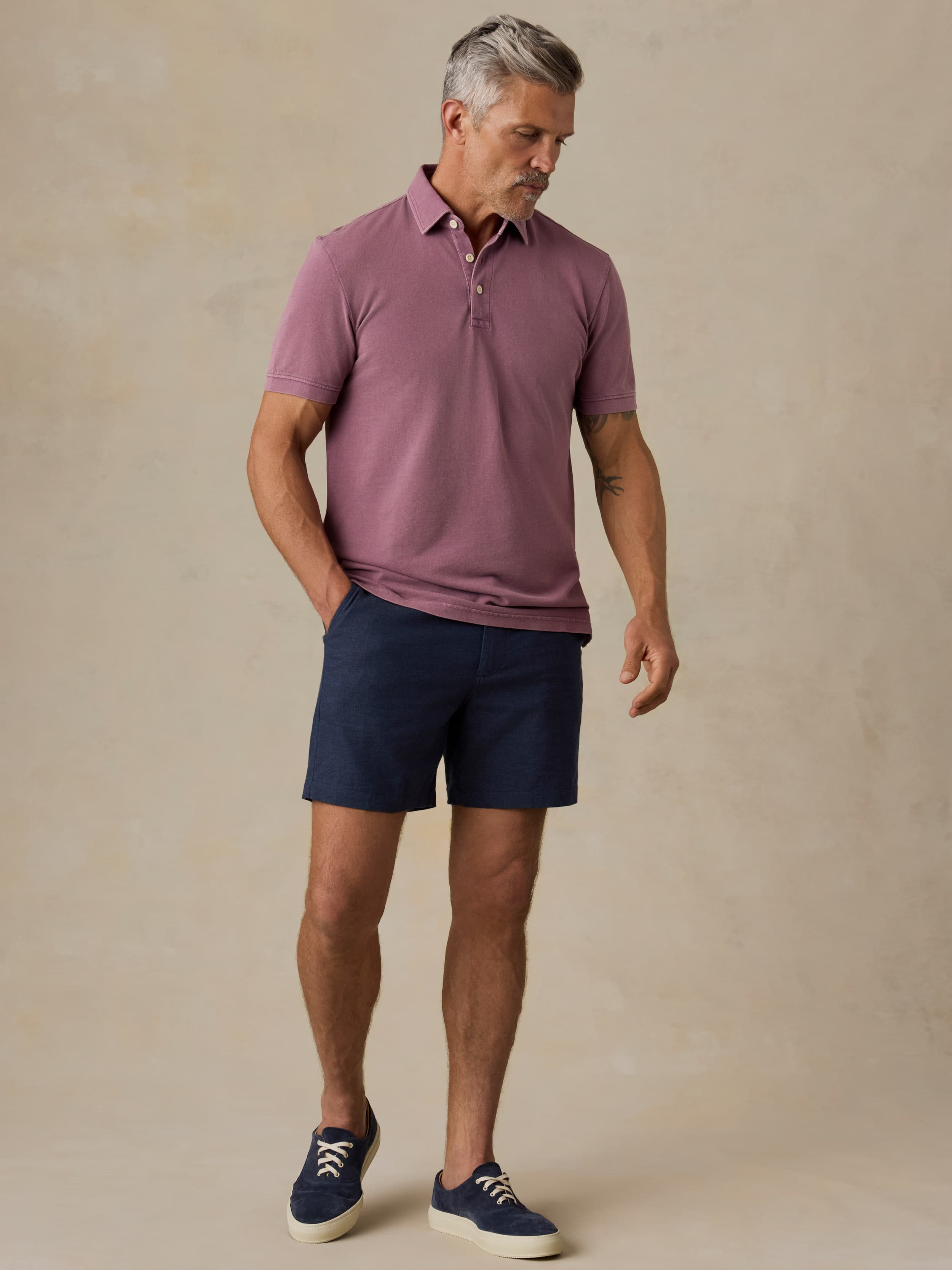 Man wearing a purple polo shirt and navy shorts against a beige background