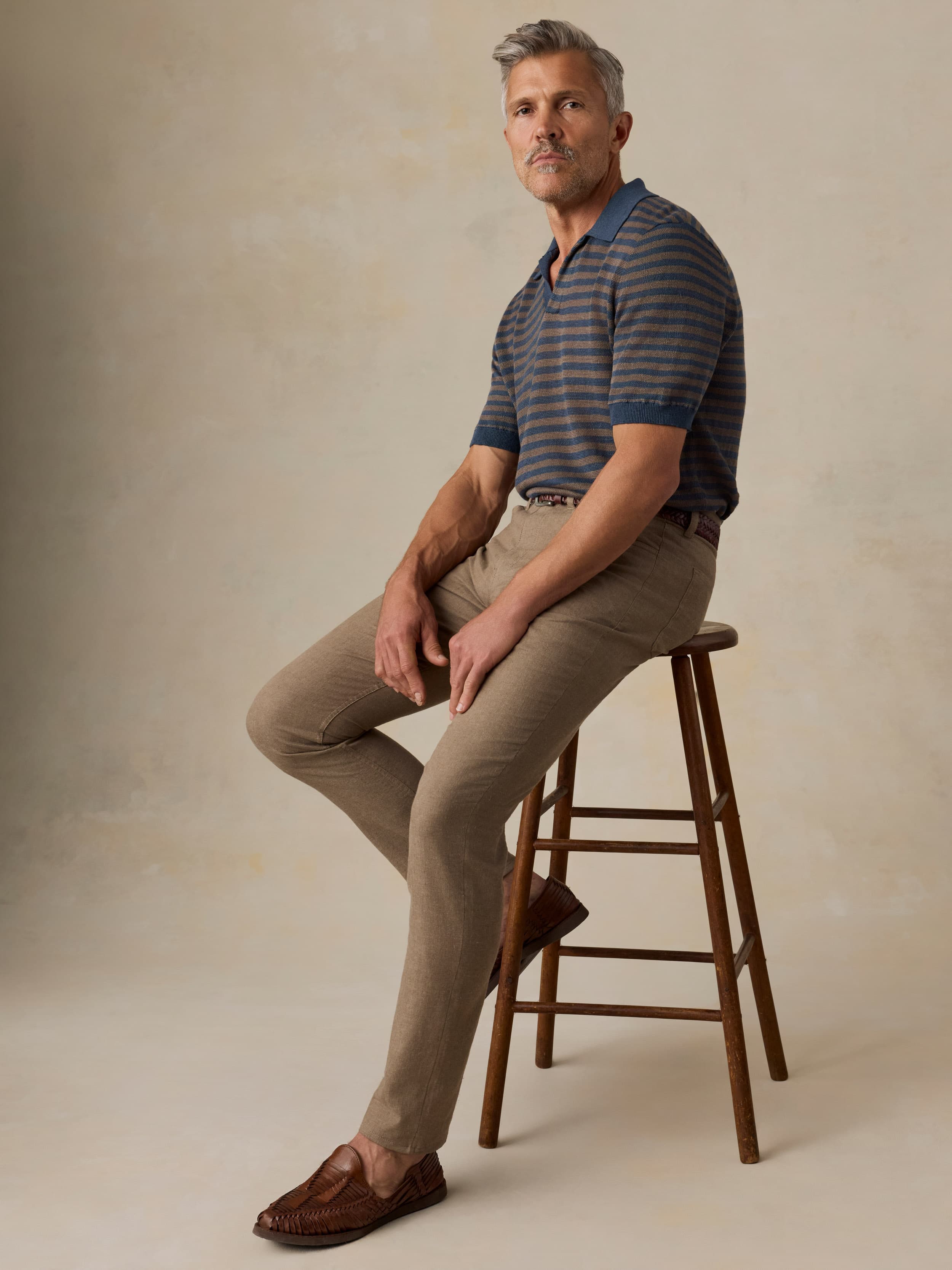 Man wearing green pants and a striped tee against a beige background