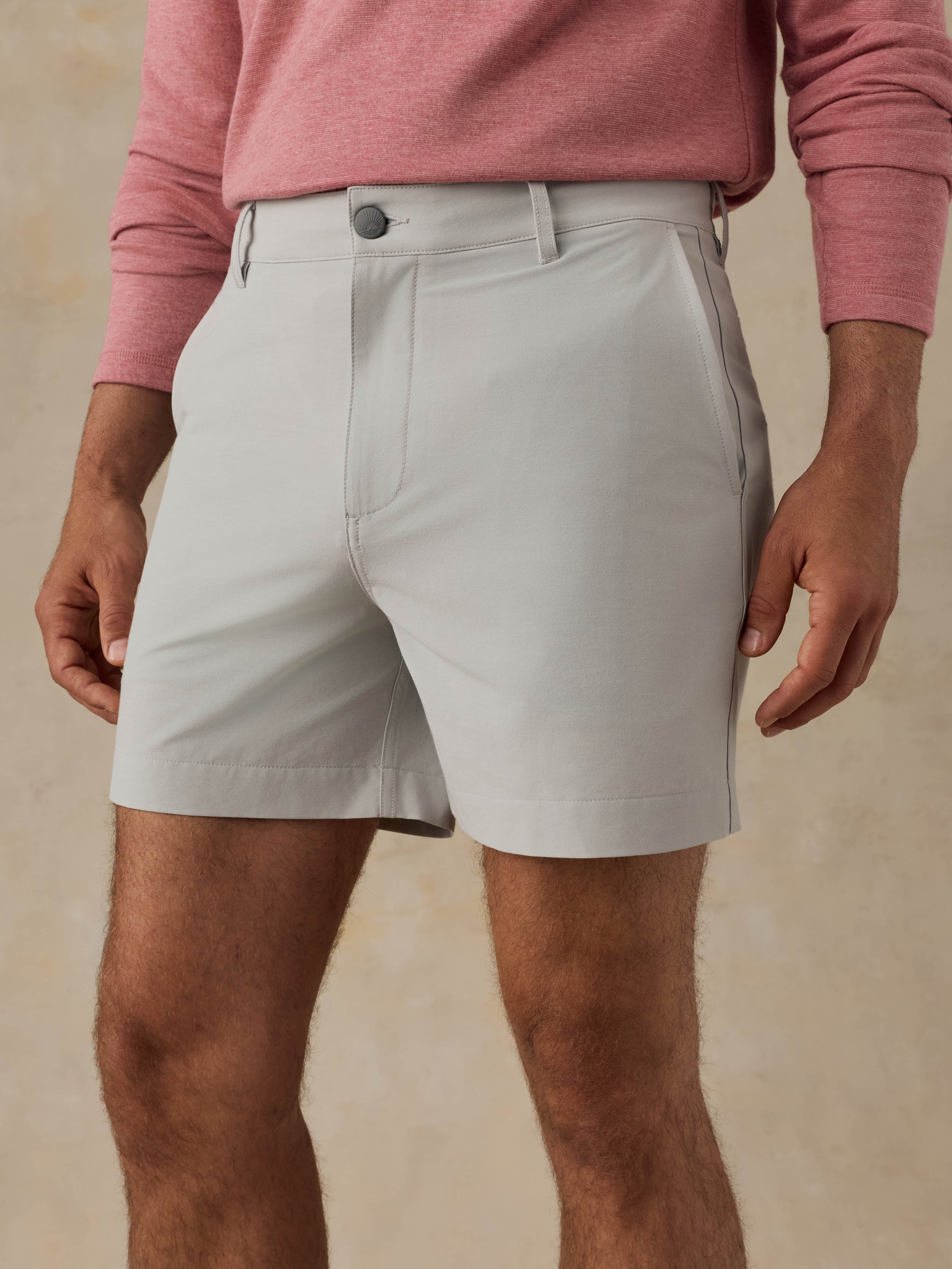Man is wearing grey shorts and a red crewneck against a beige background