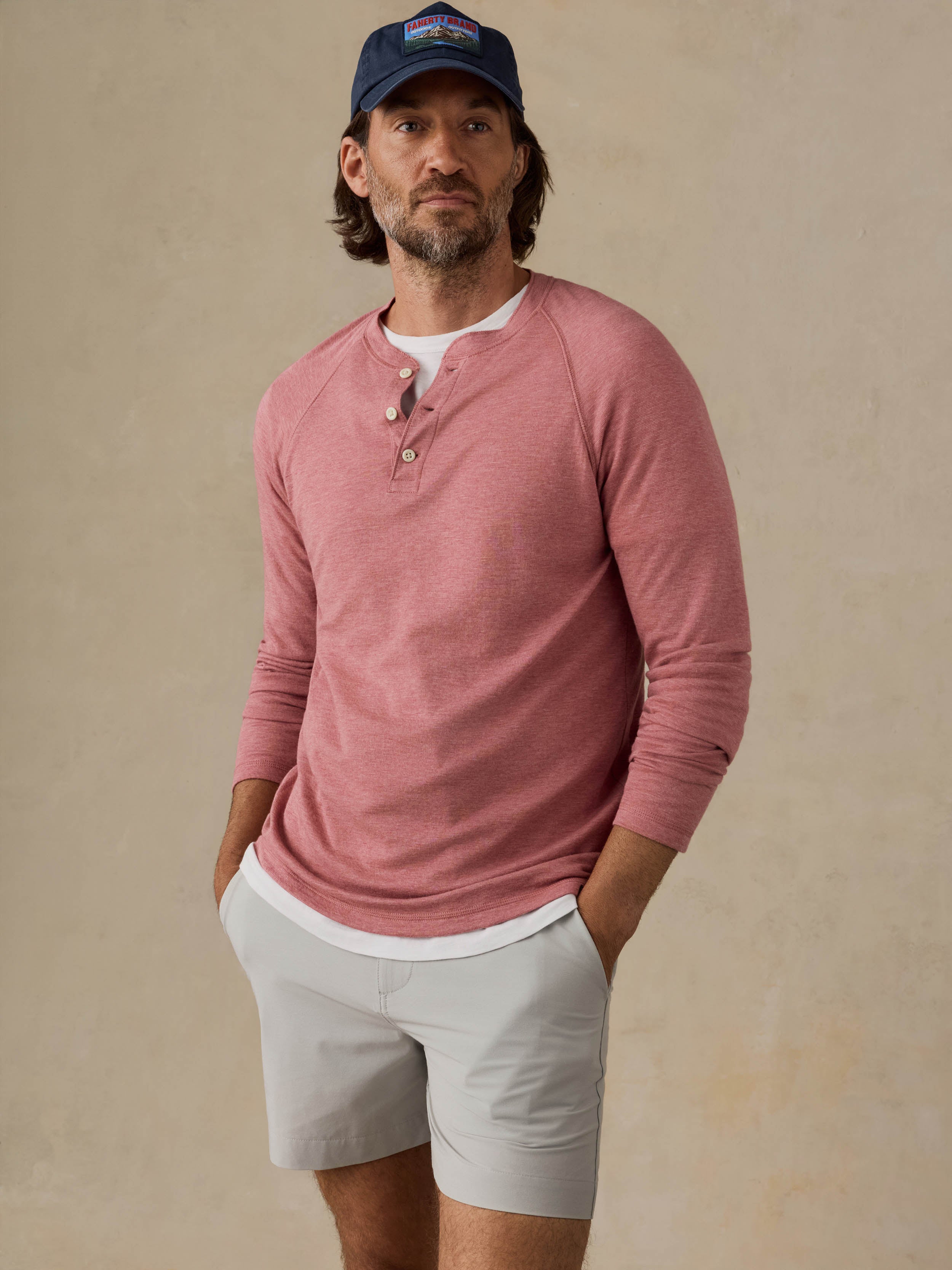 Man is wearing grey shorts and a red henley against a beige background