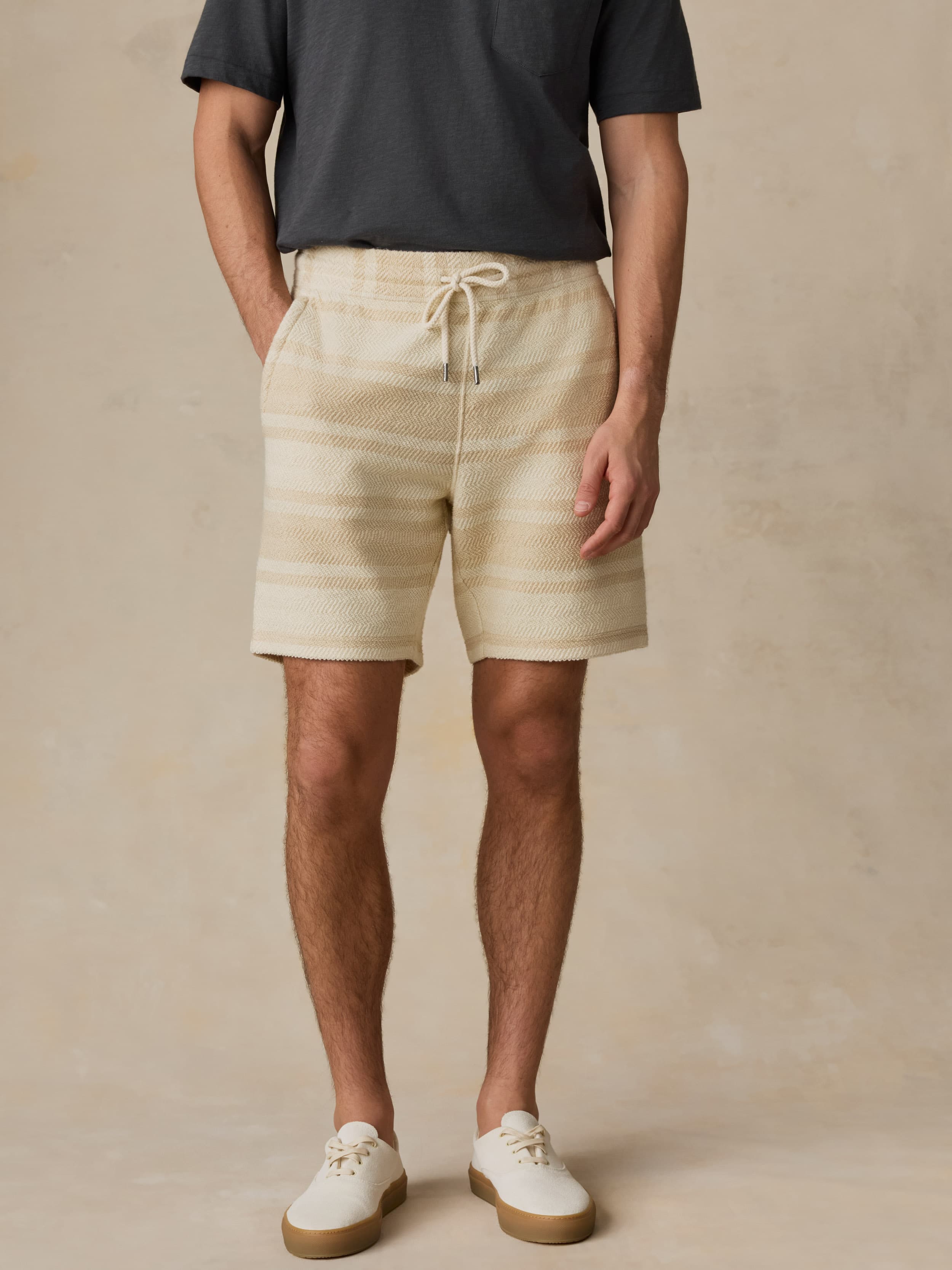Man wearing beige striped shorts and a black shirt on a beige background