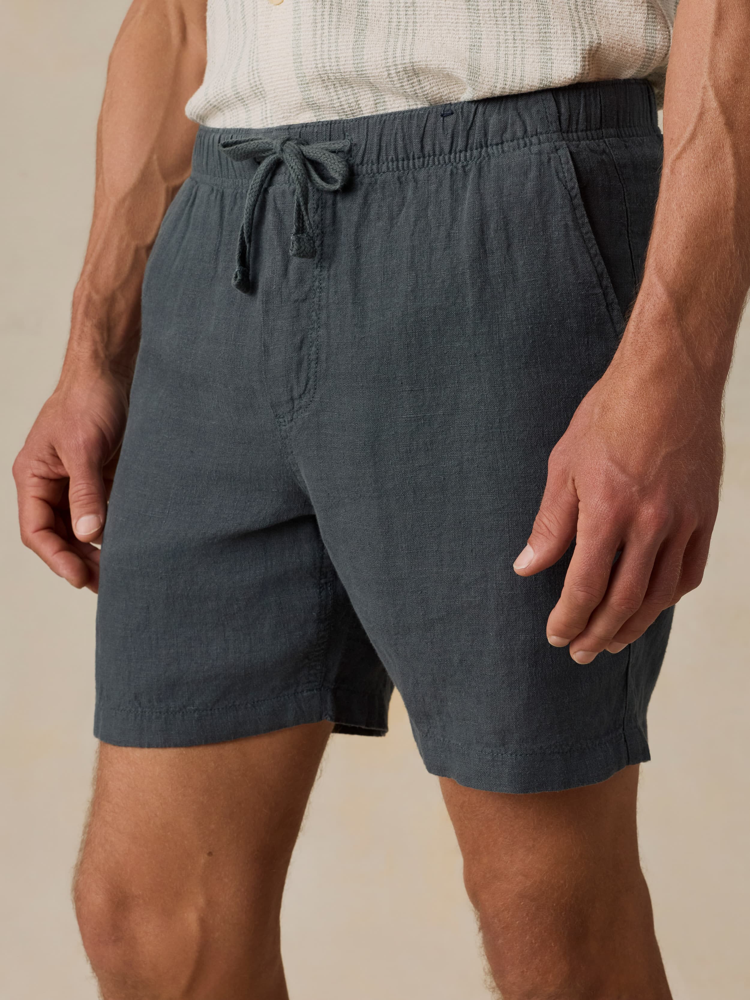 Man wearing a light-colored shirt and black linen shorts against a beige background