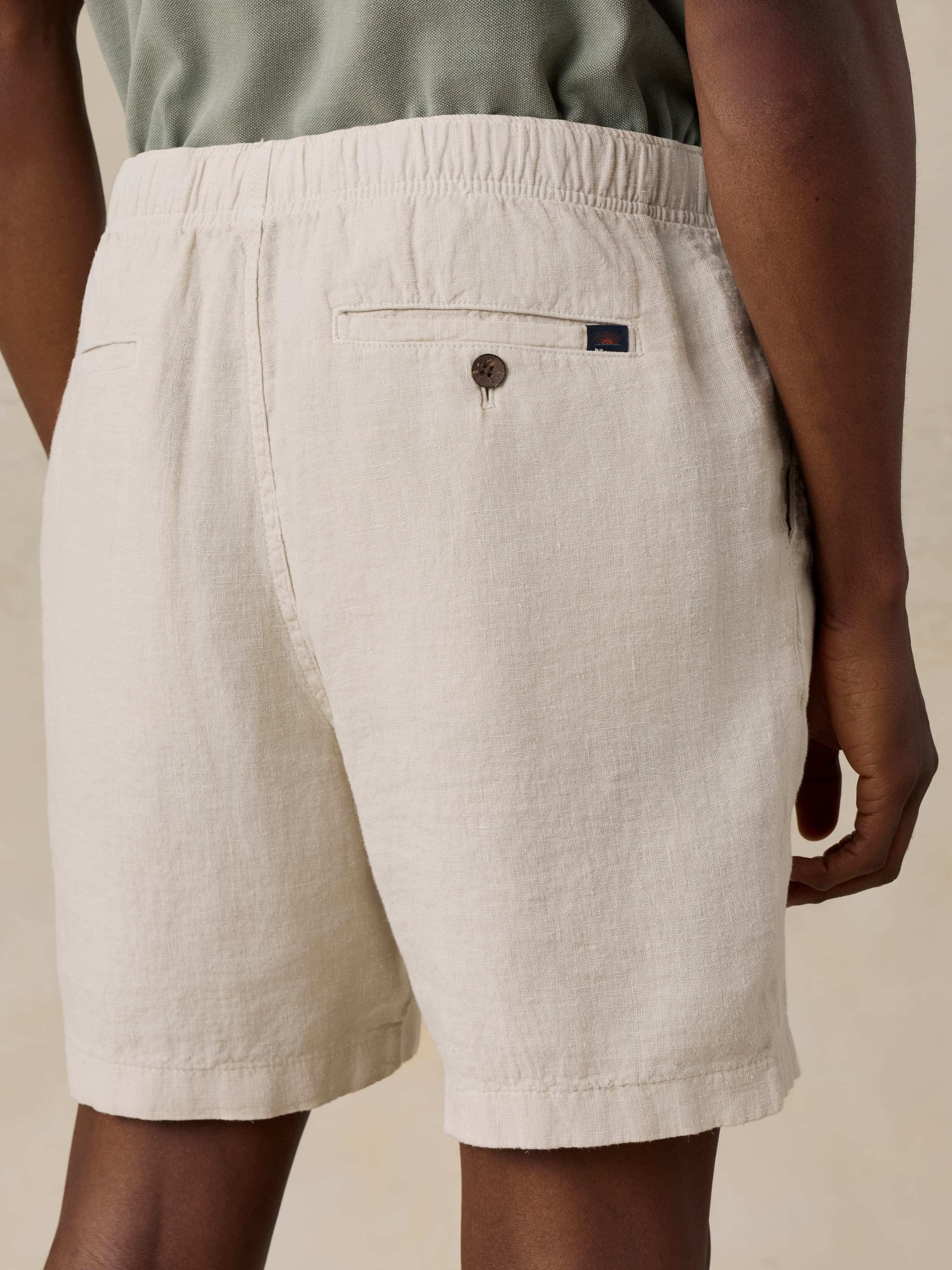 Beige linen shorts worn by a man on a neutral background