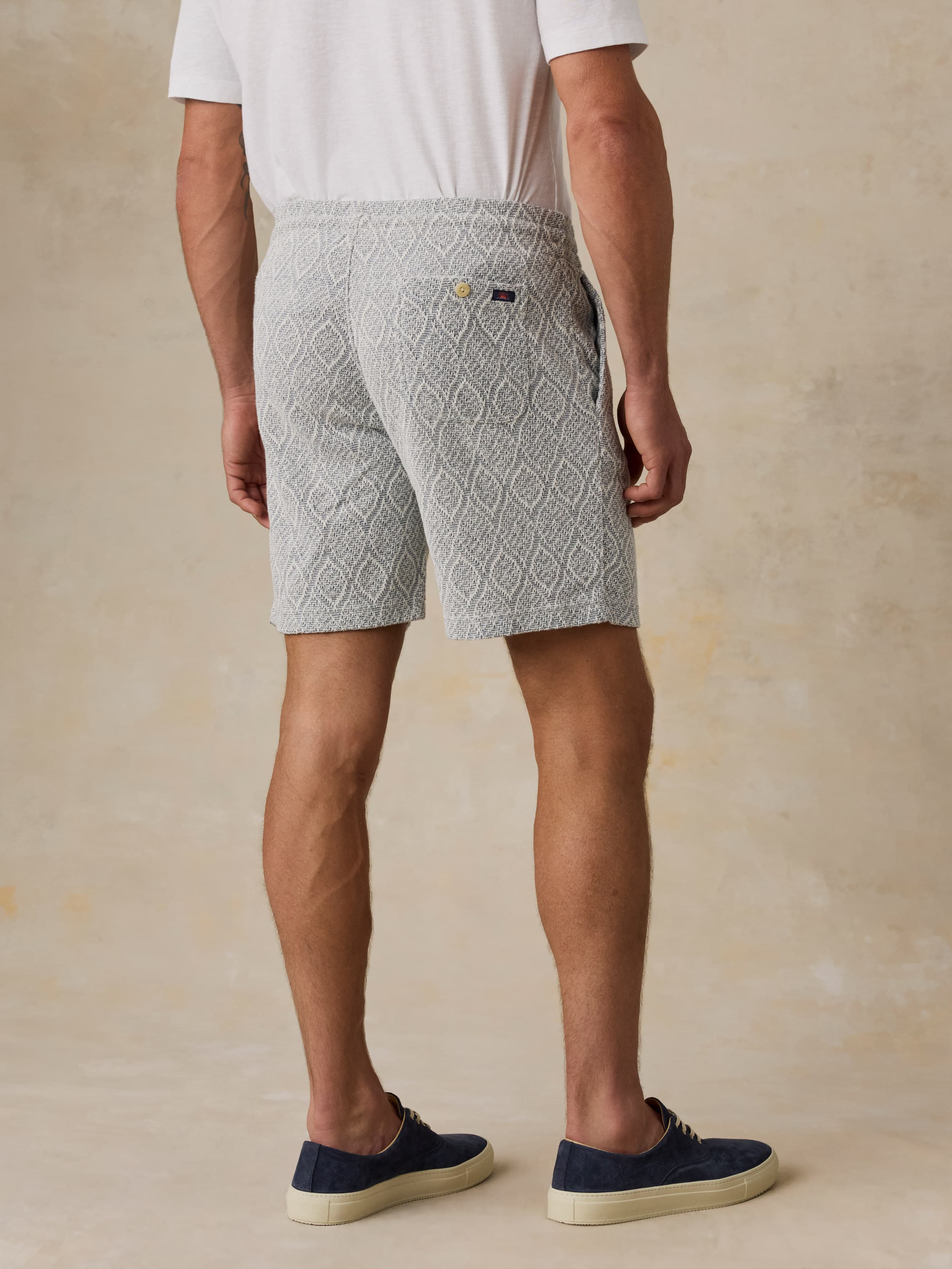 Man wearing blue printed shorts and a white t-shirt against a beige background