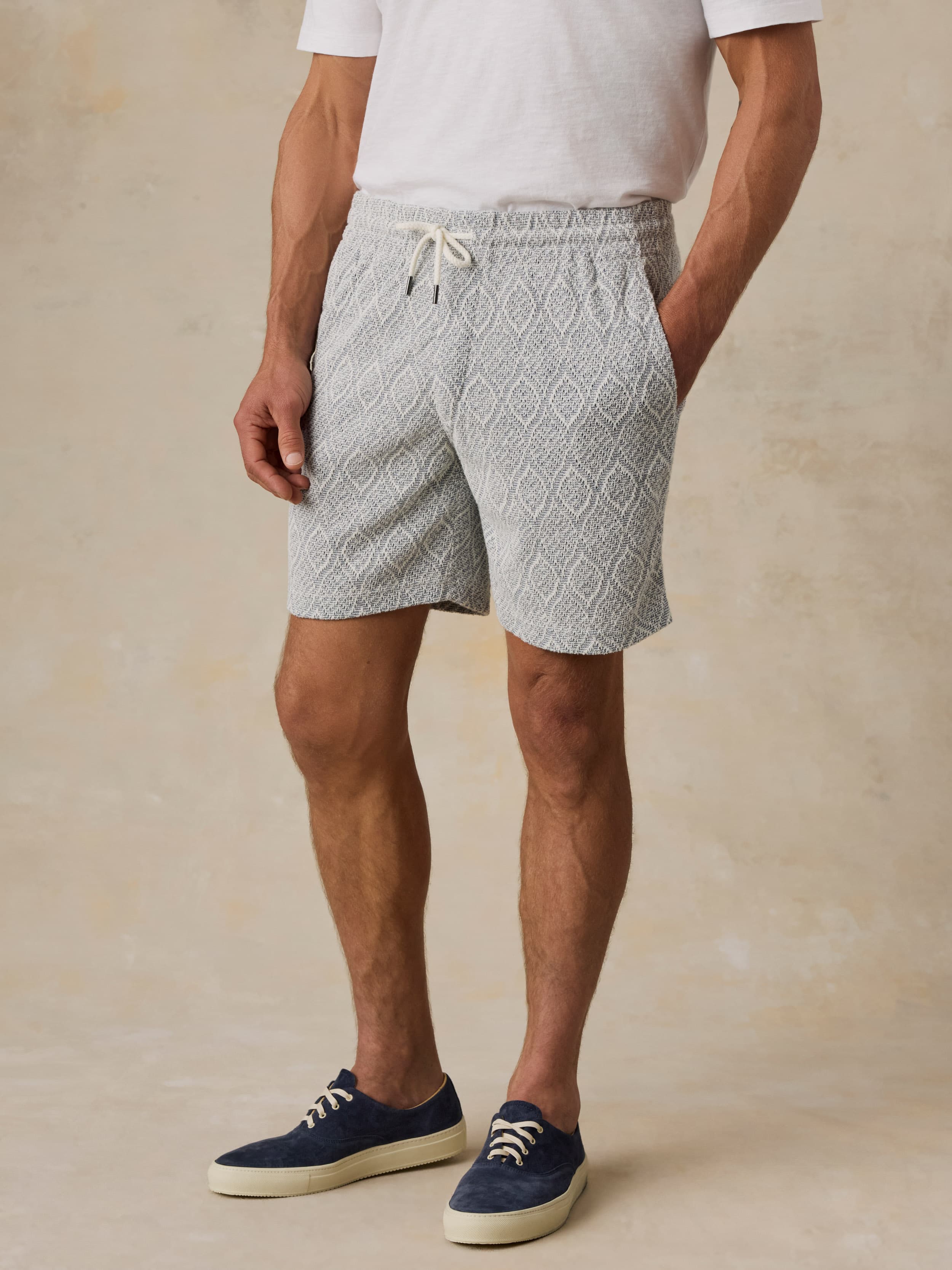 Man wearing blue printed shorts and a white t-shirt against a beige background