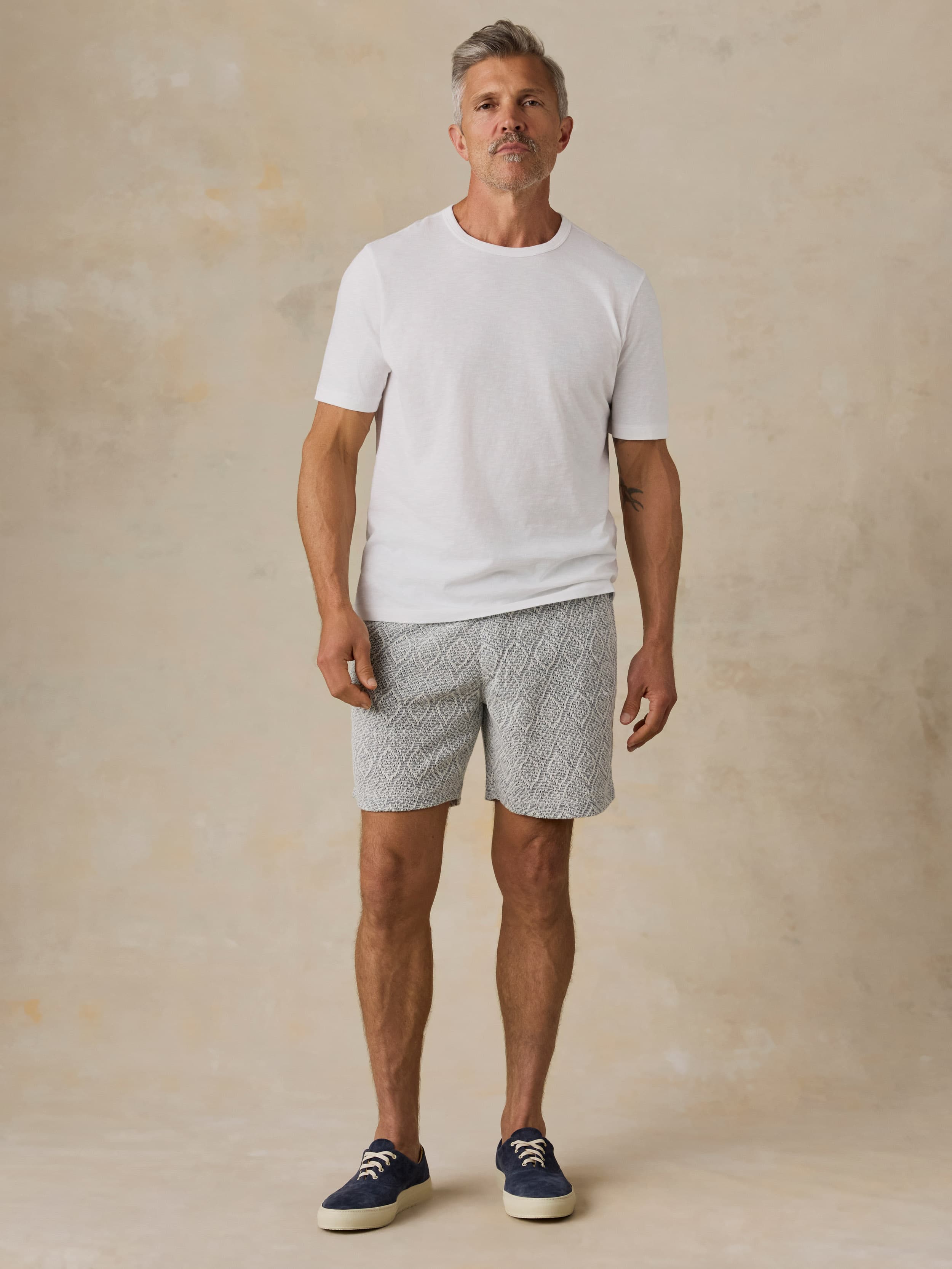 Man wearing blue printed shorts and a white t-shirt against a beige background