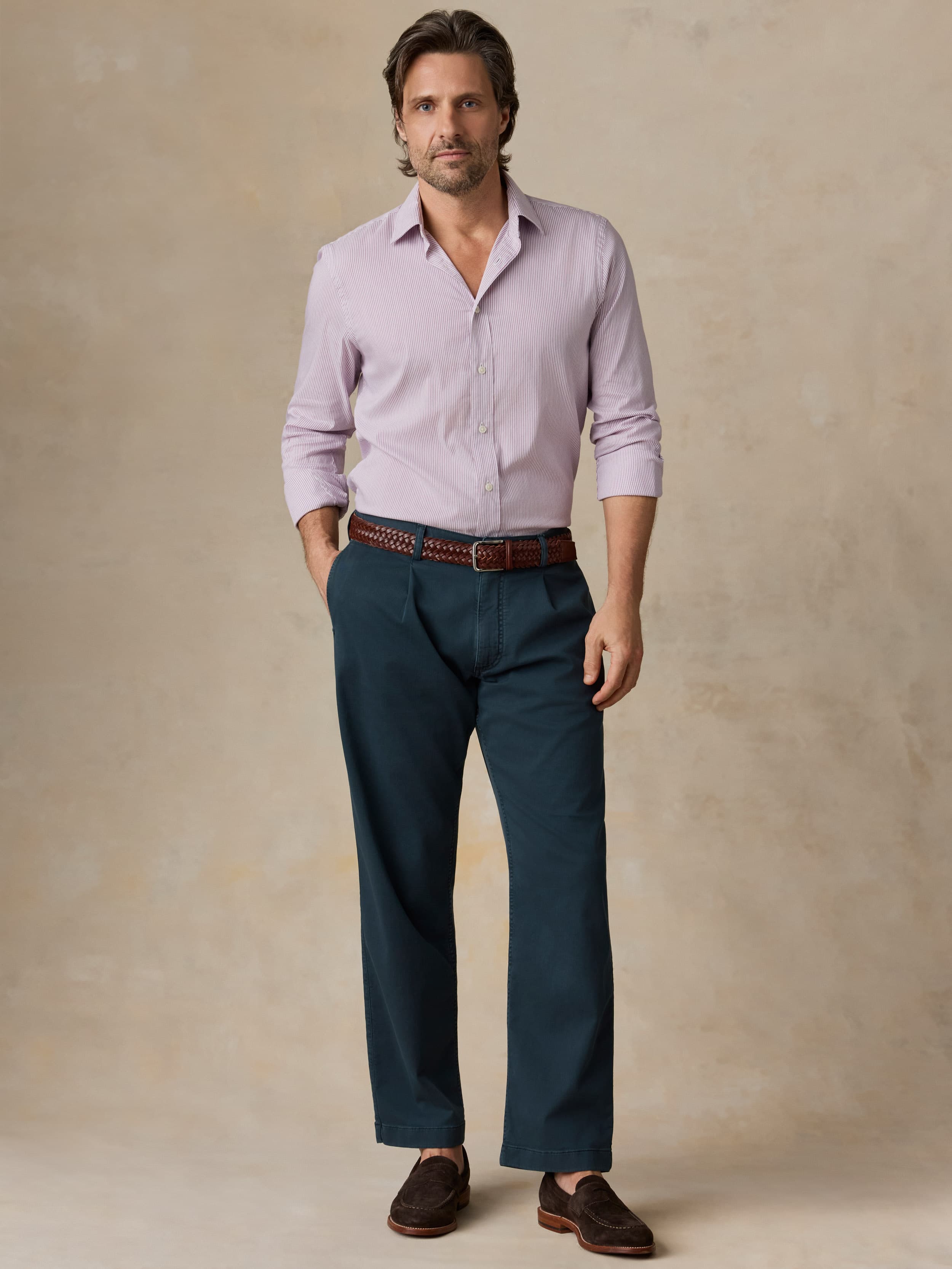 Man wearing navy pants with a purple button-down shirt against a beige background