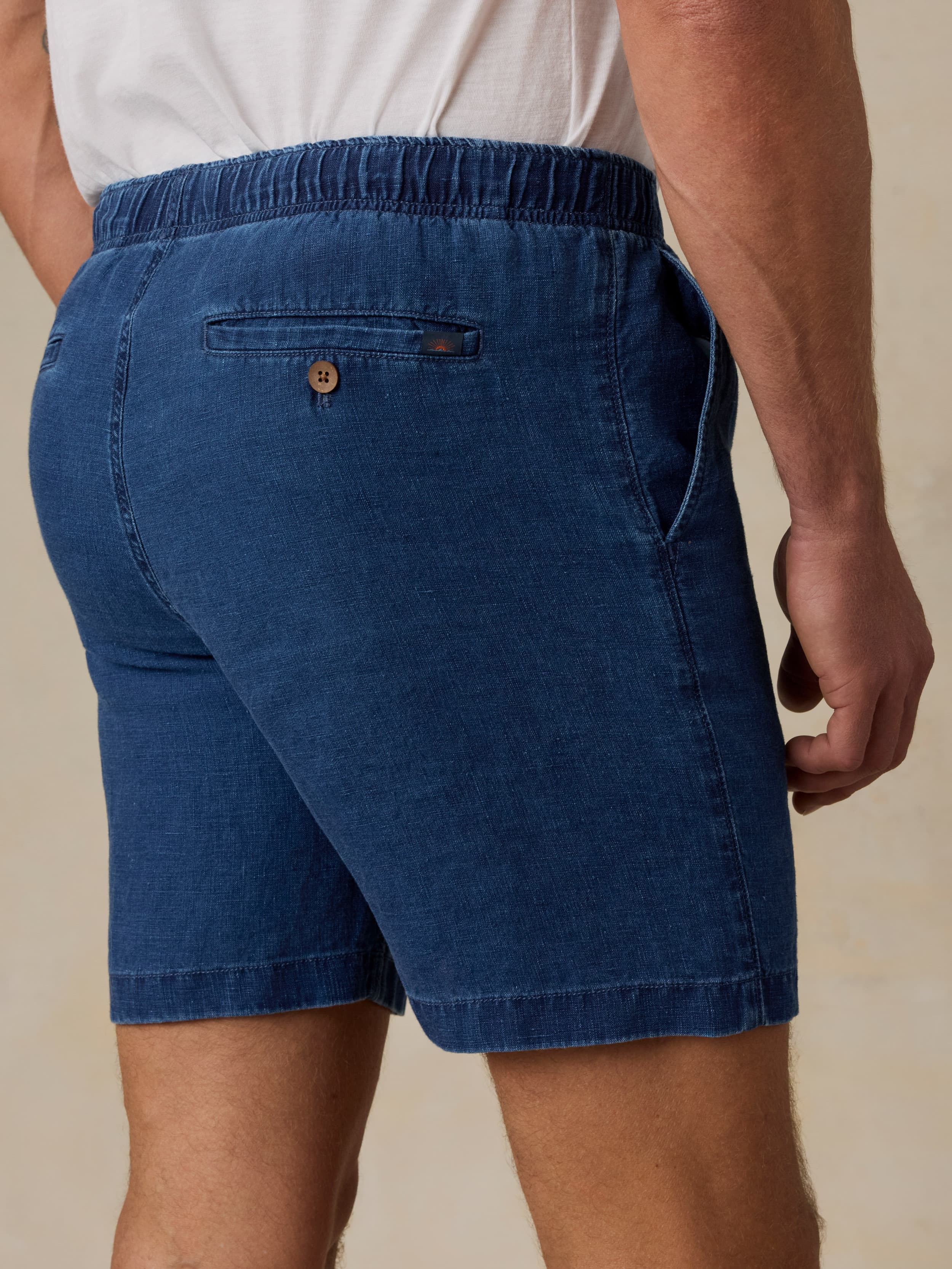 Man wearing navy linen shorts against a beige background
