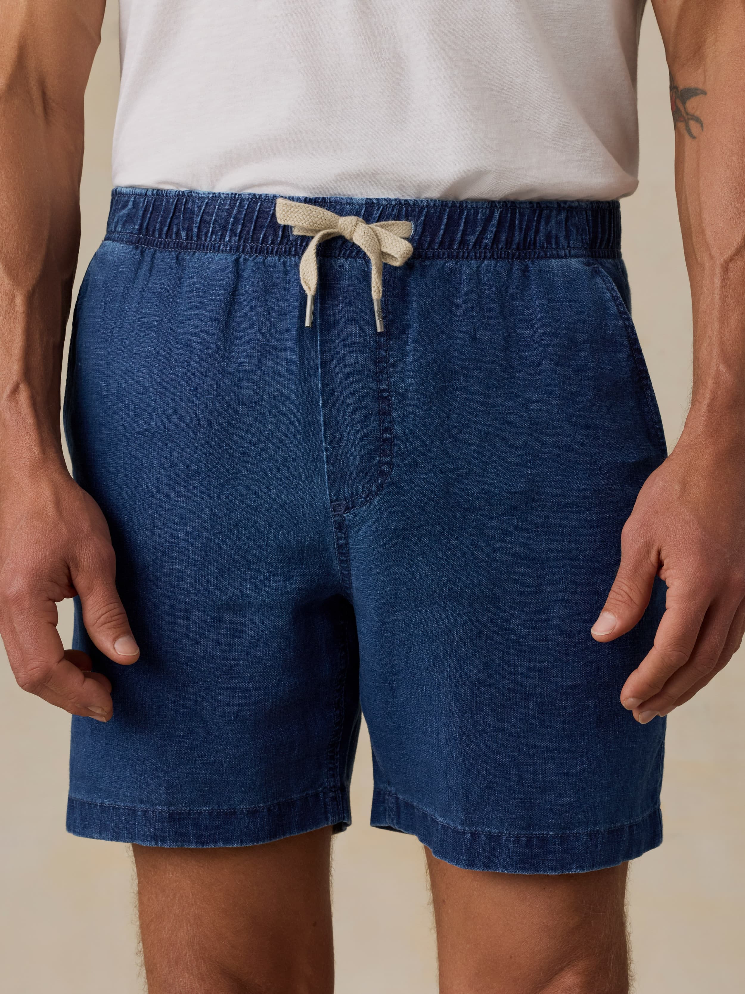 Man wearing navy linen shorts against a beige background