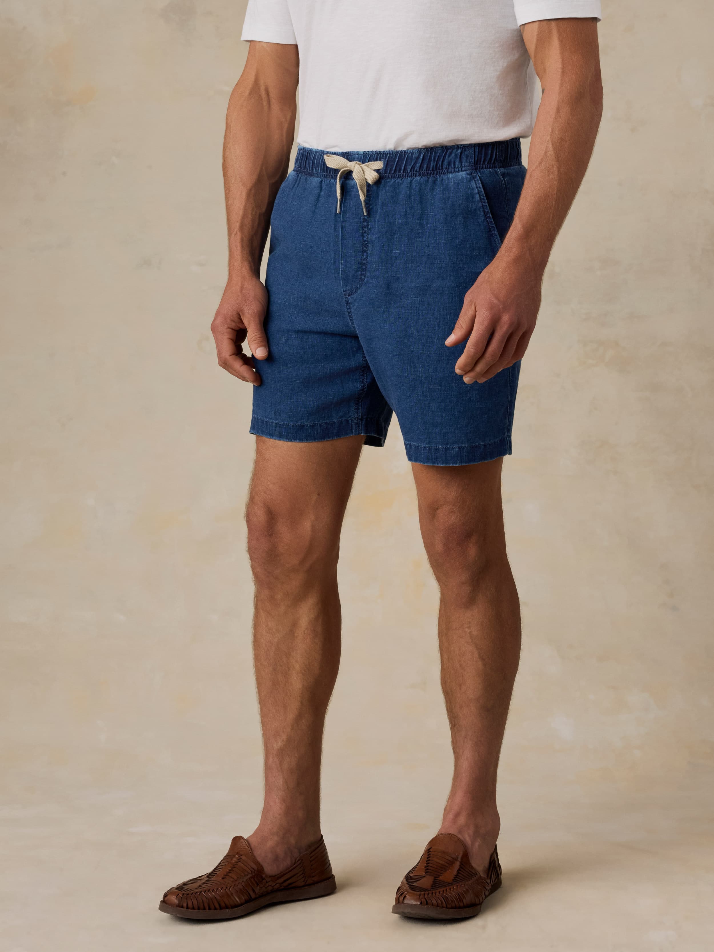 Person wearing blue linen shorts and a white t-shirt on a beige background