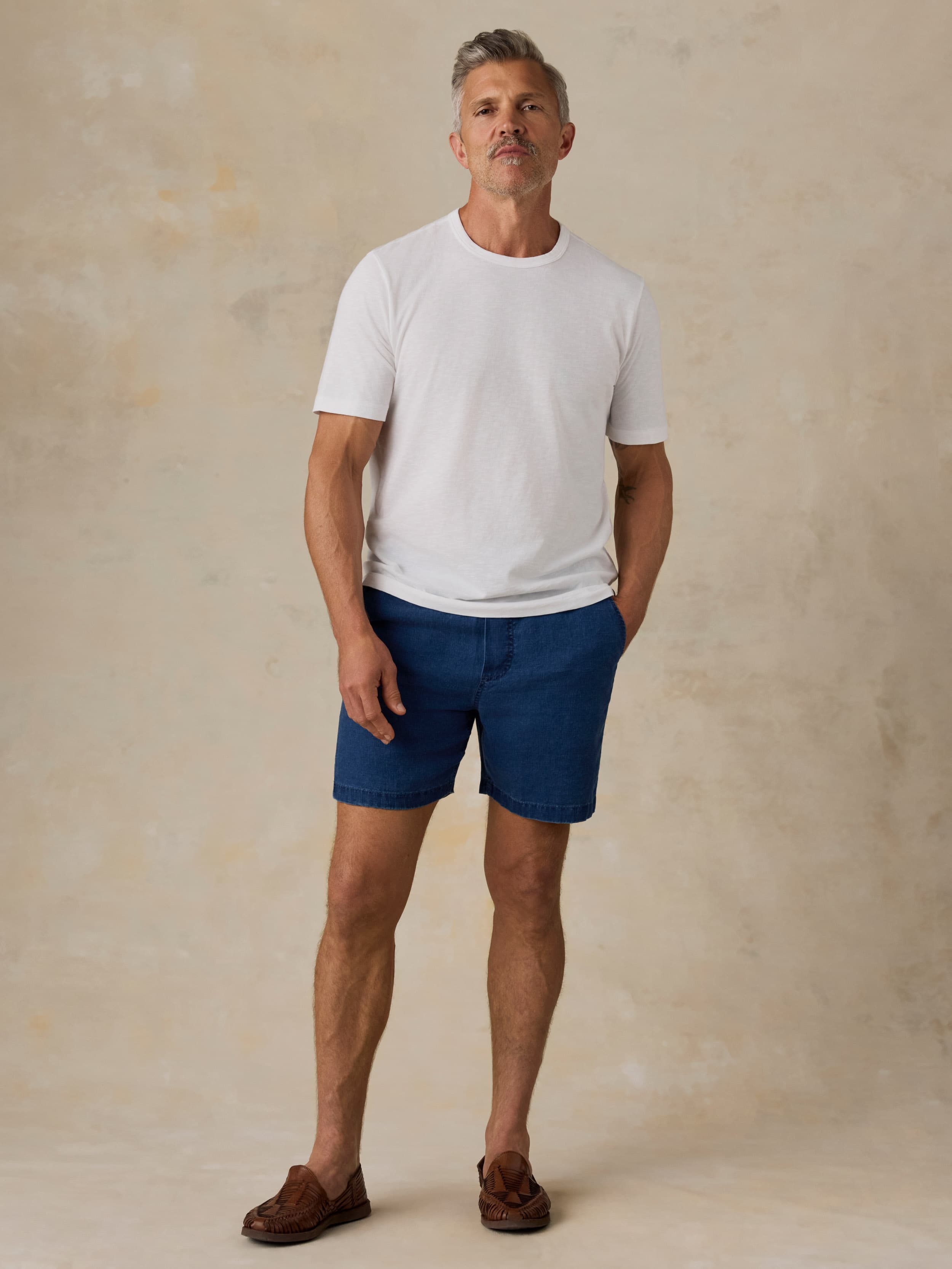 Man wearing a white t-shirt and blue linen shorts against a beige background