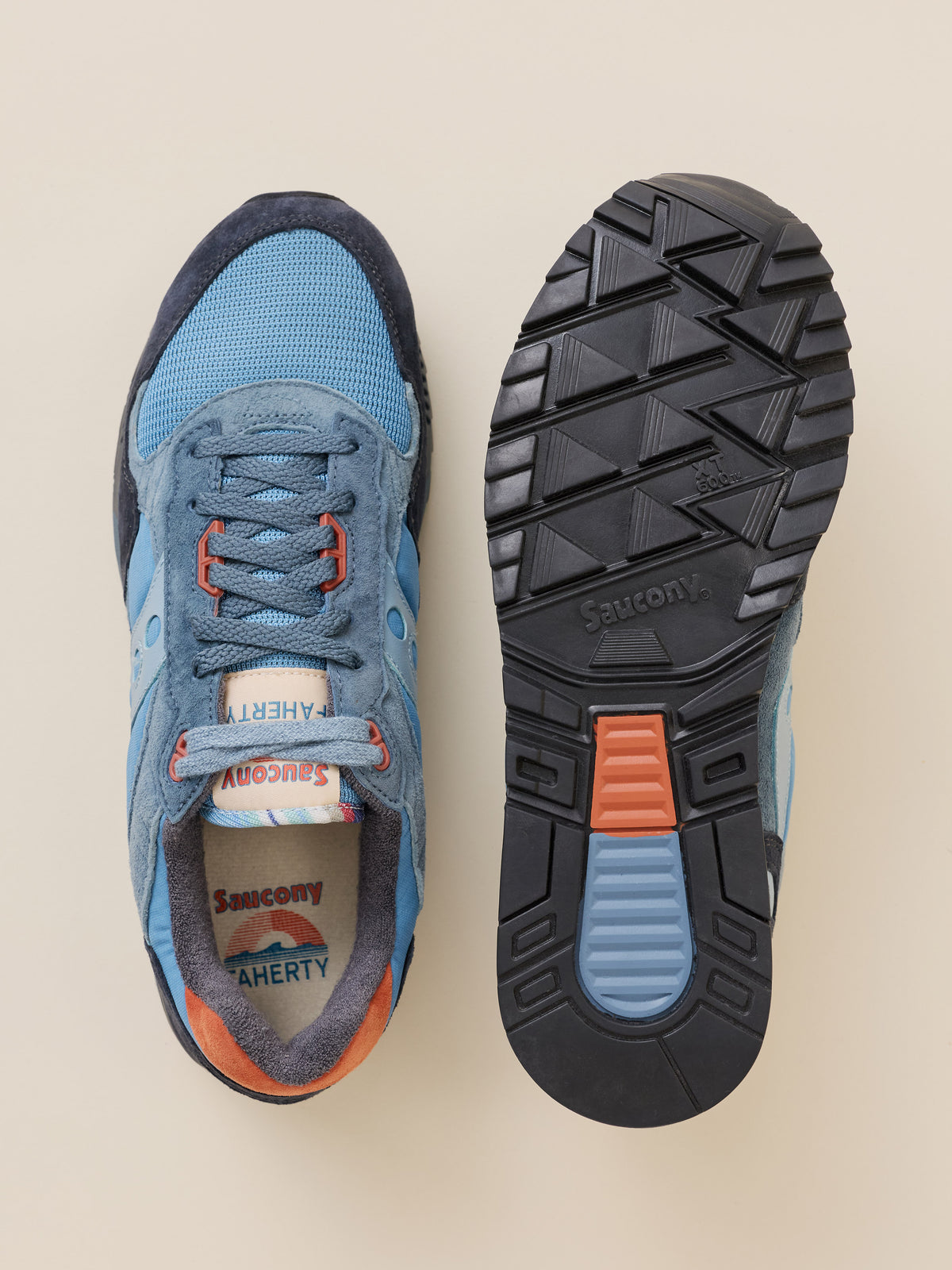 A pair of Faherty x Saucony sneakers shown from a top-down view, displaying the blue suede and mesh upper on one shoe and the black treaded outsole on the other, set against a solid beige background., image 4 of 4
