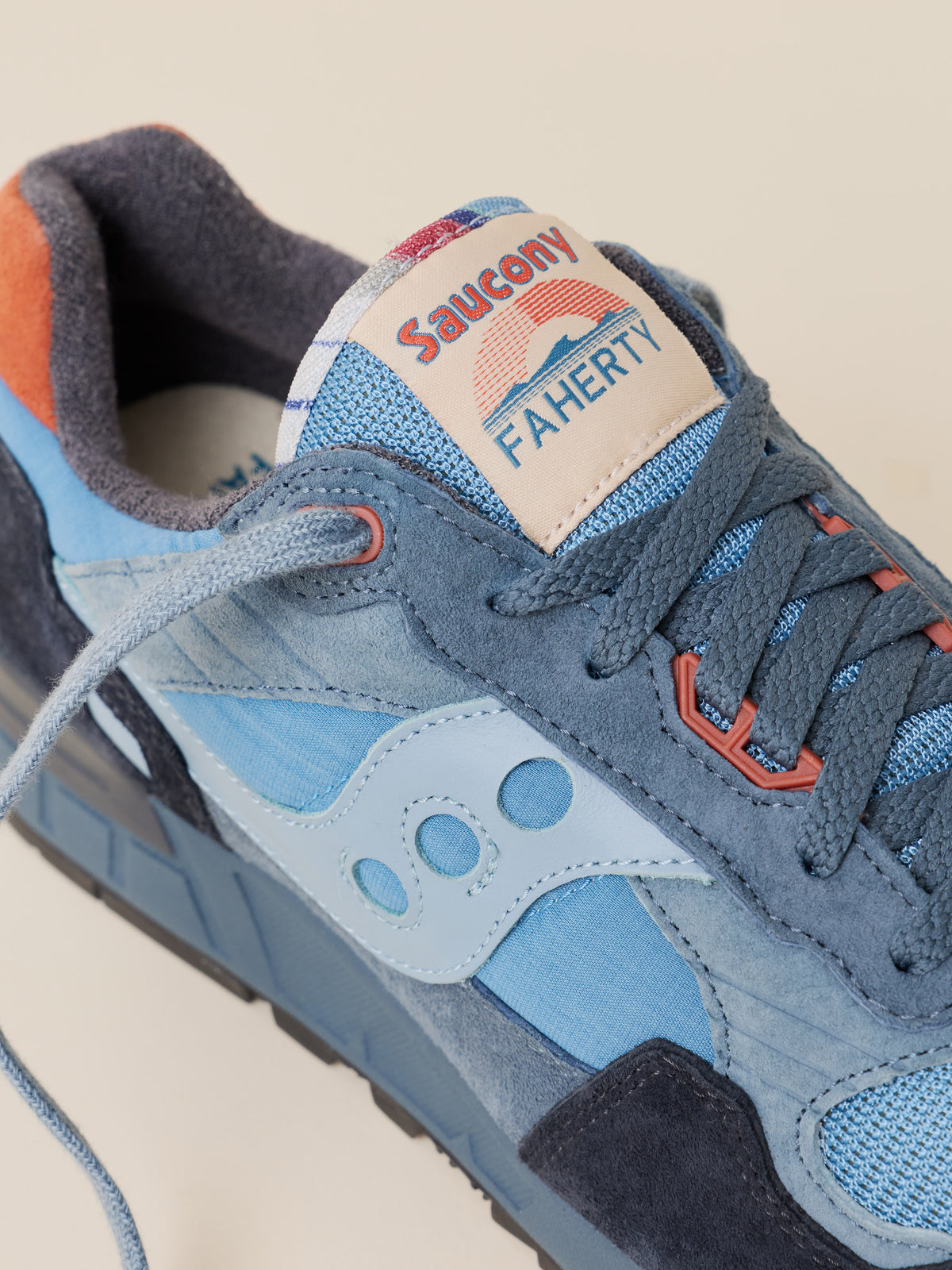 Close-up of a Faherty x Saucony sneaker in blue suede and mesh with light blue overlays, dark navy suede panels, and orange-red accents on the laces and tongue label., image 3 of 4