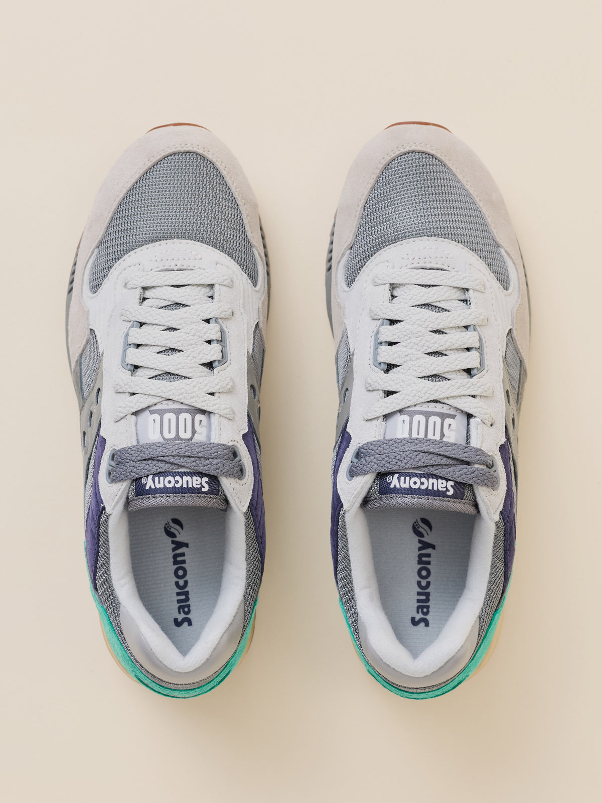 A pair of Saucony 500 sneakers shown from a top-down view on a light beige background. The shoes feature a white and gray mesh upper with gray overlays, white laces, and a small teal accent on the heel.