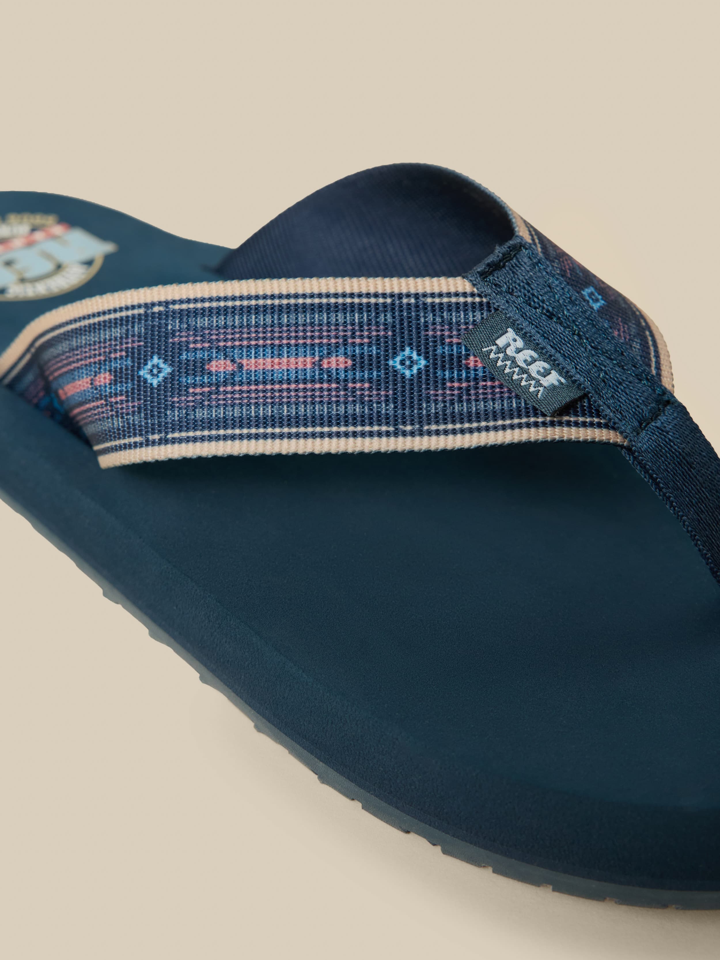 Pair of blue flip-flops with a Faherty x REEF brand logo on a beige background
