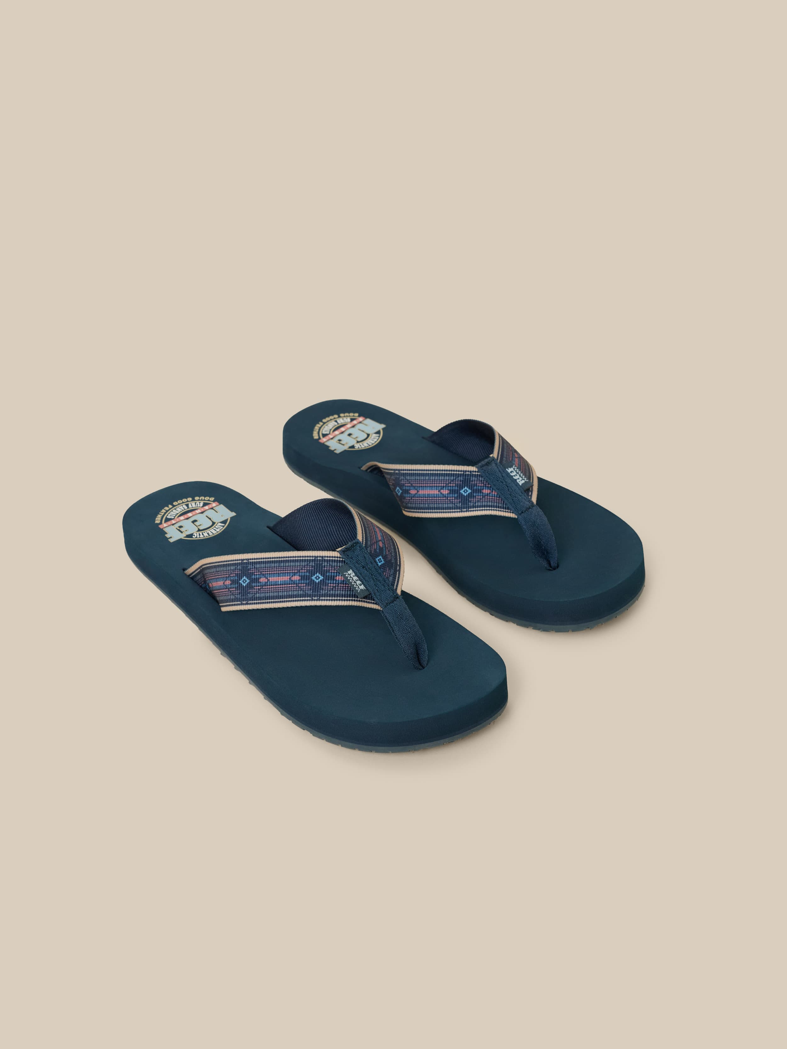 Pair of blue flip-flops with a Faherty x REEF brand logo on a beige background