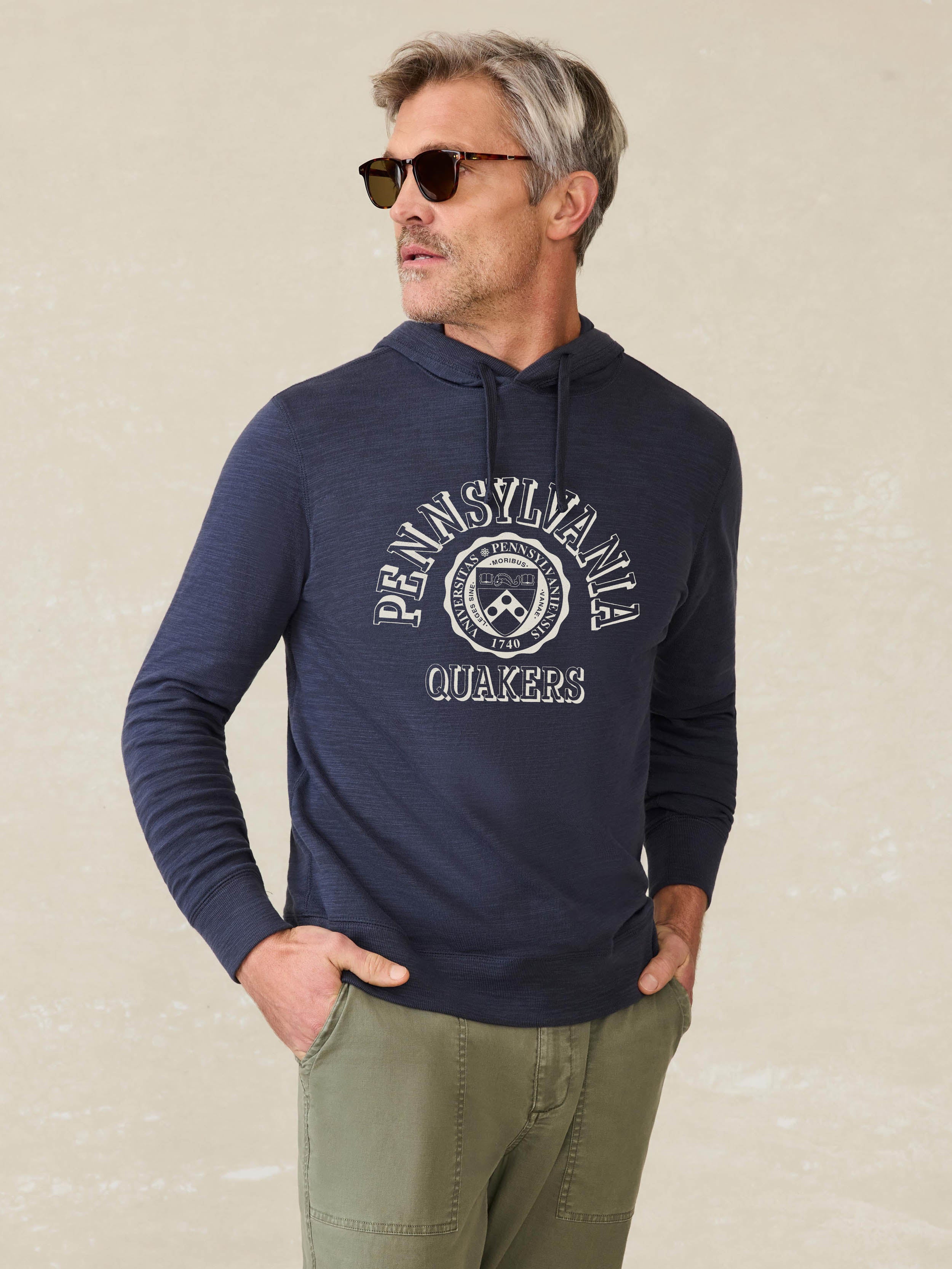 Man is wearing a navy blue hoodie with University of Pennsylvania graphic on the front against a beige background