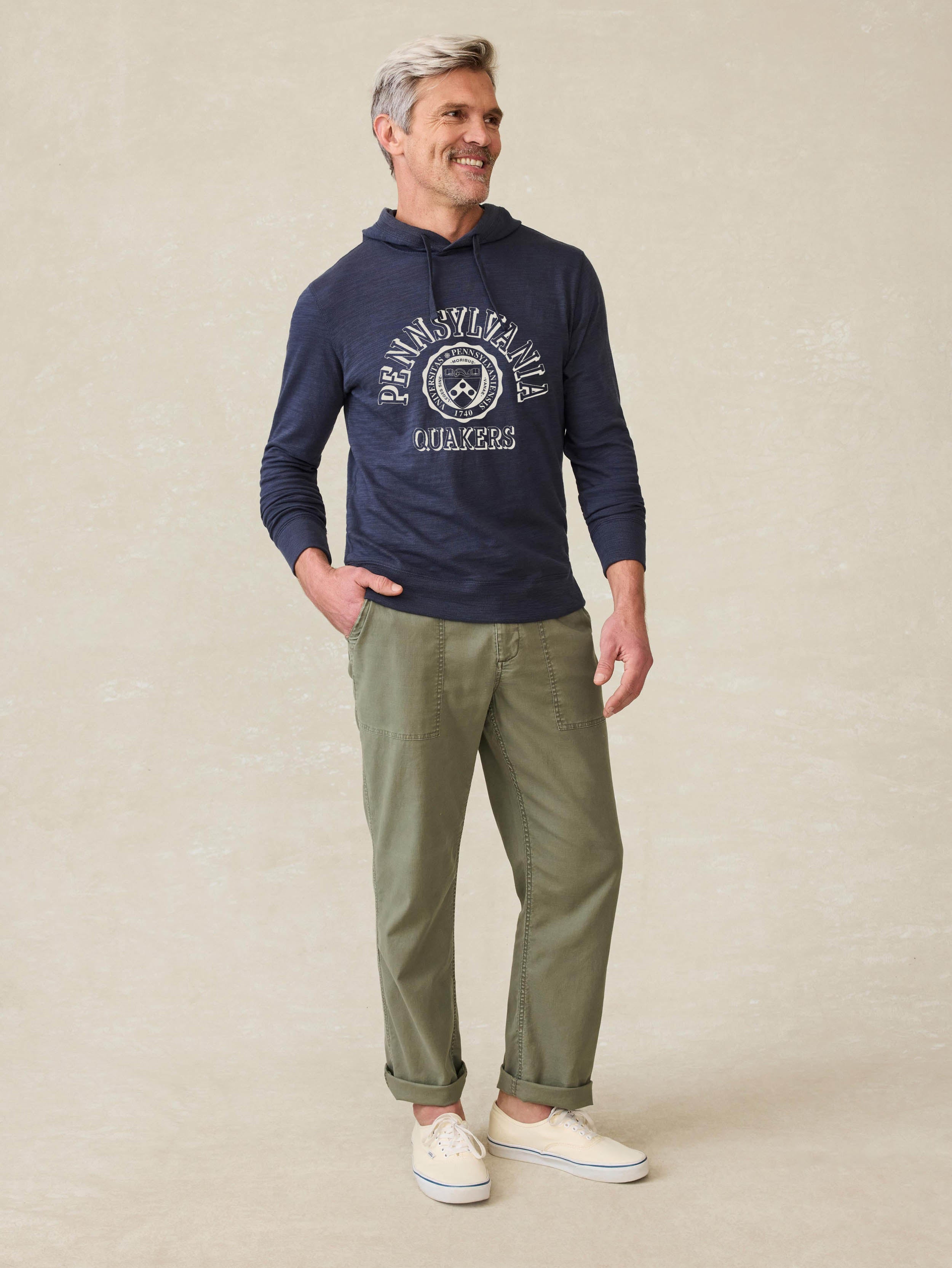 Man is wearing a navy blue hoodie with University of Pennsylvania graphic on the front against a beige background
