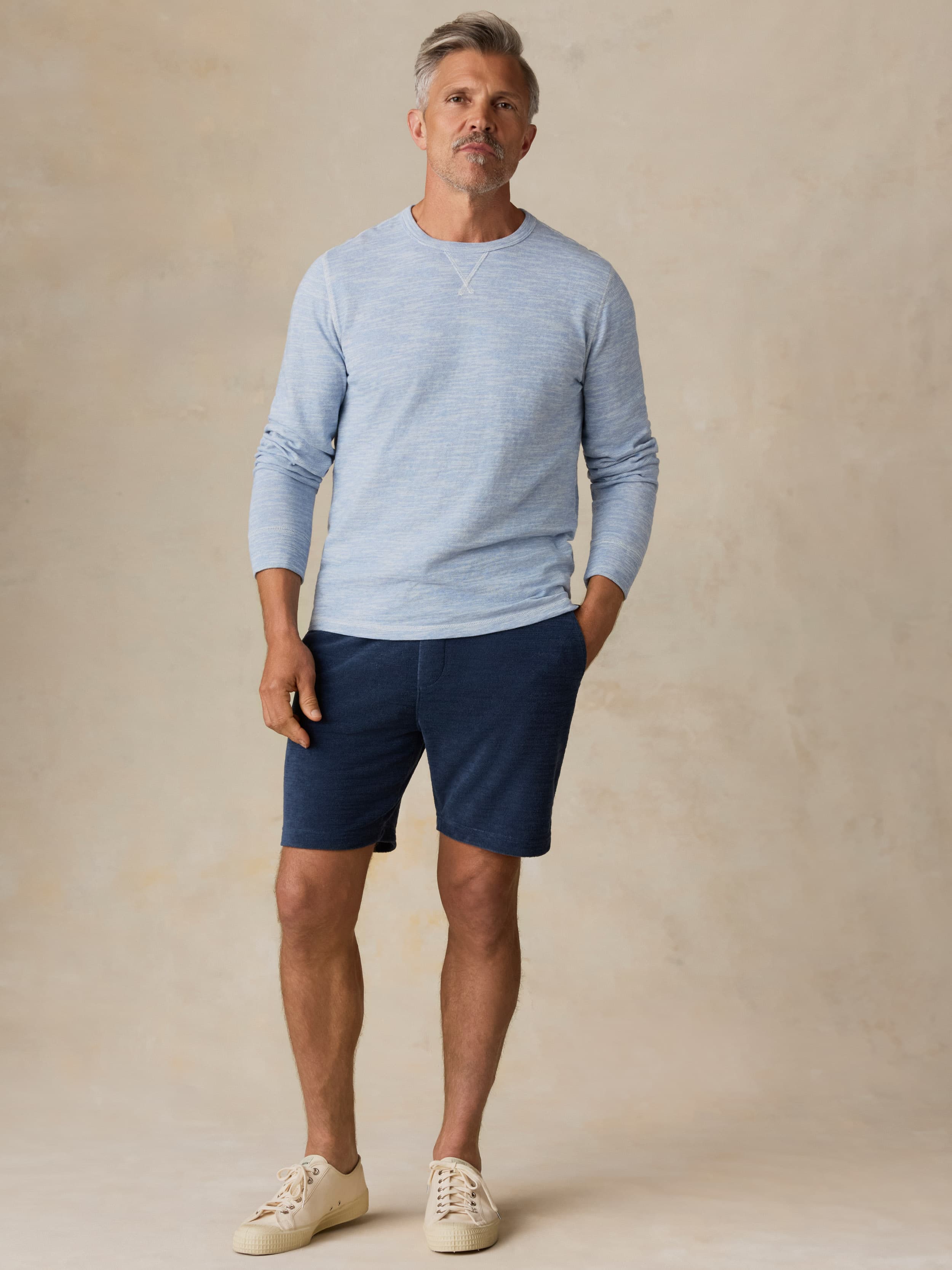 Man wearing a light blue crewneck and navy shorts against a beige background
