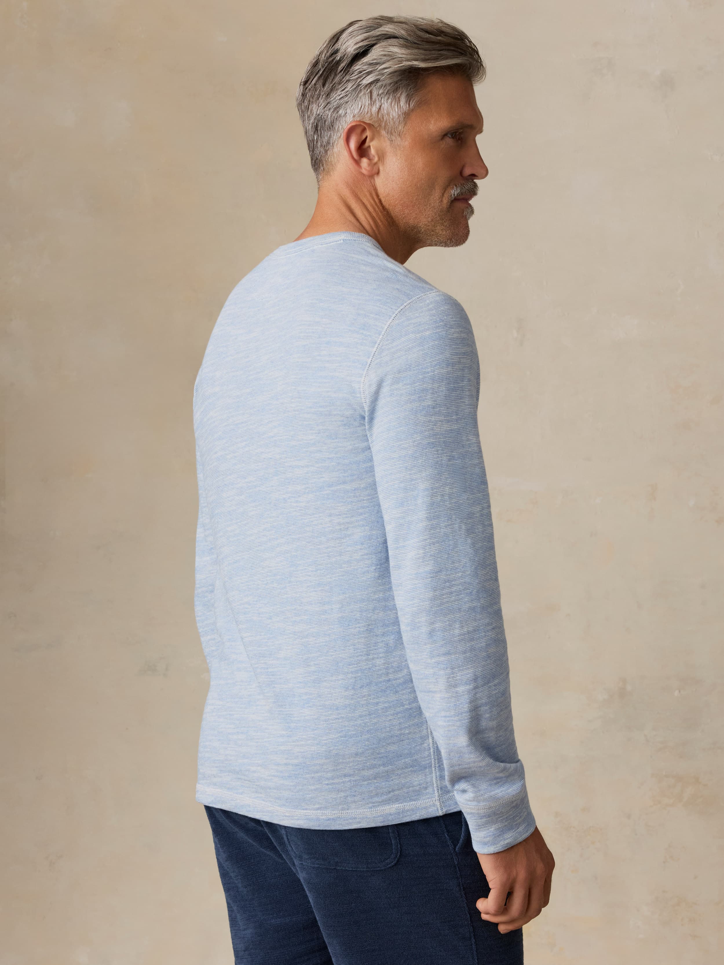 Man wearing a light blue crewneck against a beige background