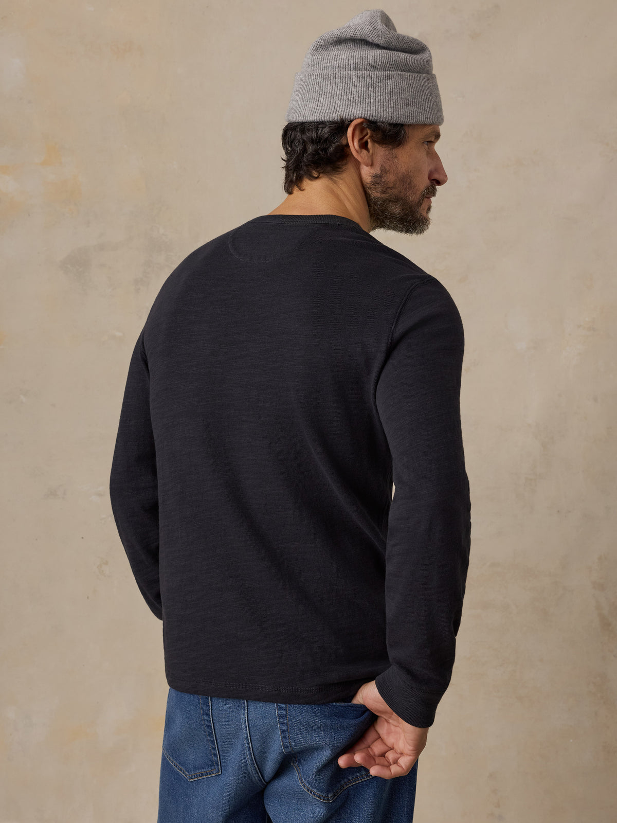 A man viewed from behind wearing a black crewneck and a beanie, image 6 of 6